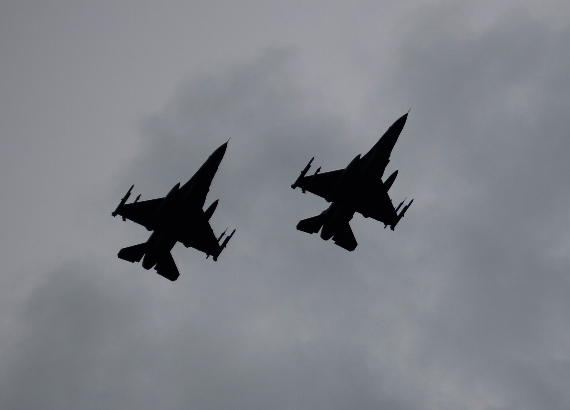 Two F-16 Fighting Falcon fighter aircraft fly over the flightline at Łask Air Base, Poland, May 7, 2014. The Fighting Falcon wields a 20mm cannon, air-to-air missiles, air-to-surface munitions and electronic countermeasure pods as part of its multirole fighter capabilities. (U.S. Air Force photo illustration by Staff Sgt. Joe W. McFadden/Released)