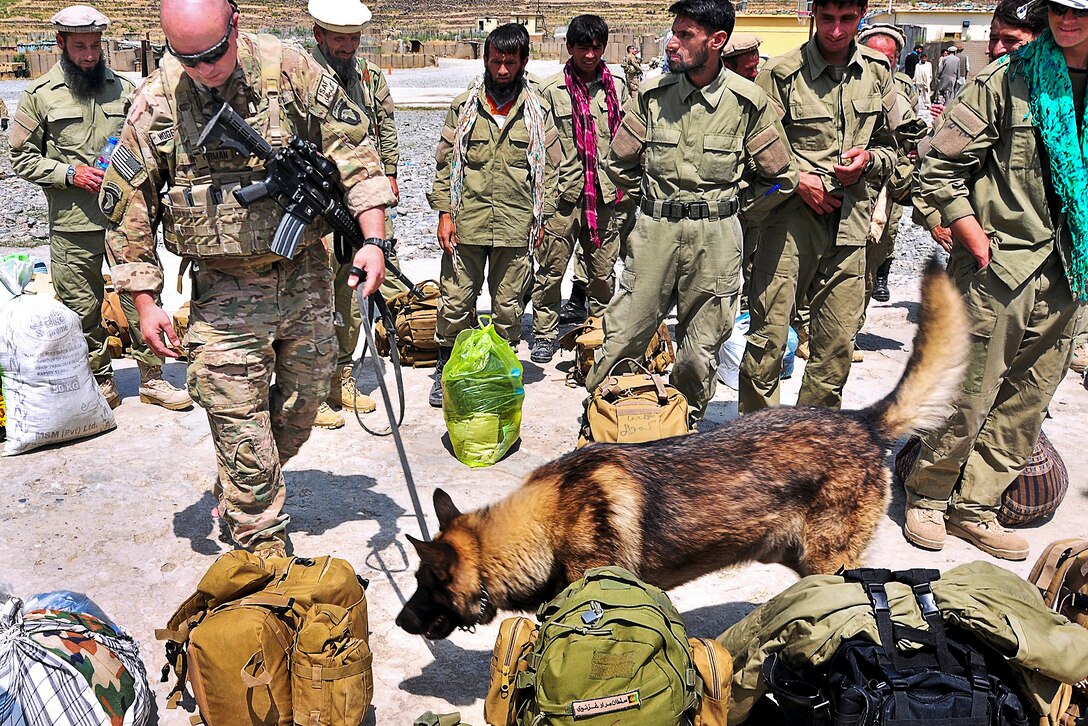 A U.S. soldier and Staff Sgt. Alex, his military working dog trained to detect explosives, search bags of recently graduated Afghan local police officers on former Forward Operating Base Bostik in Afghanistan's Kunar province, June 5, 2013. As of June 18, Afghan forces have taken the lead in providing security for their country.  
