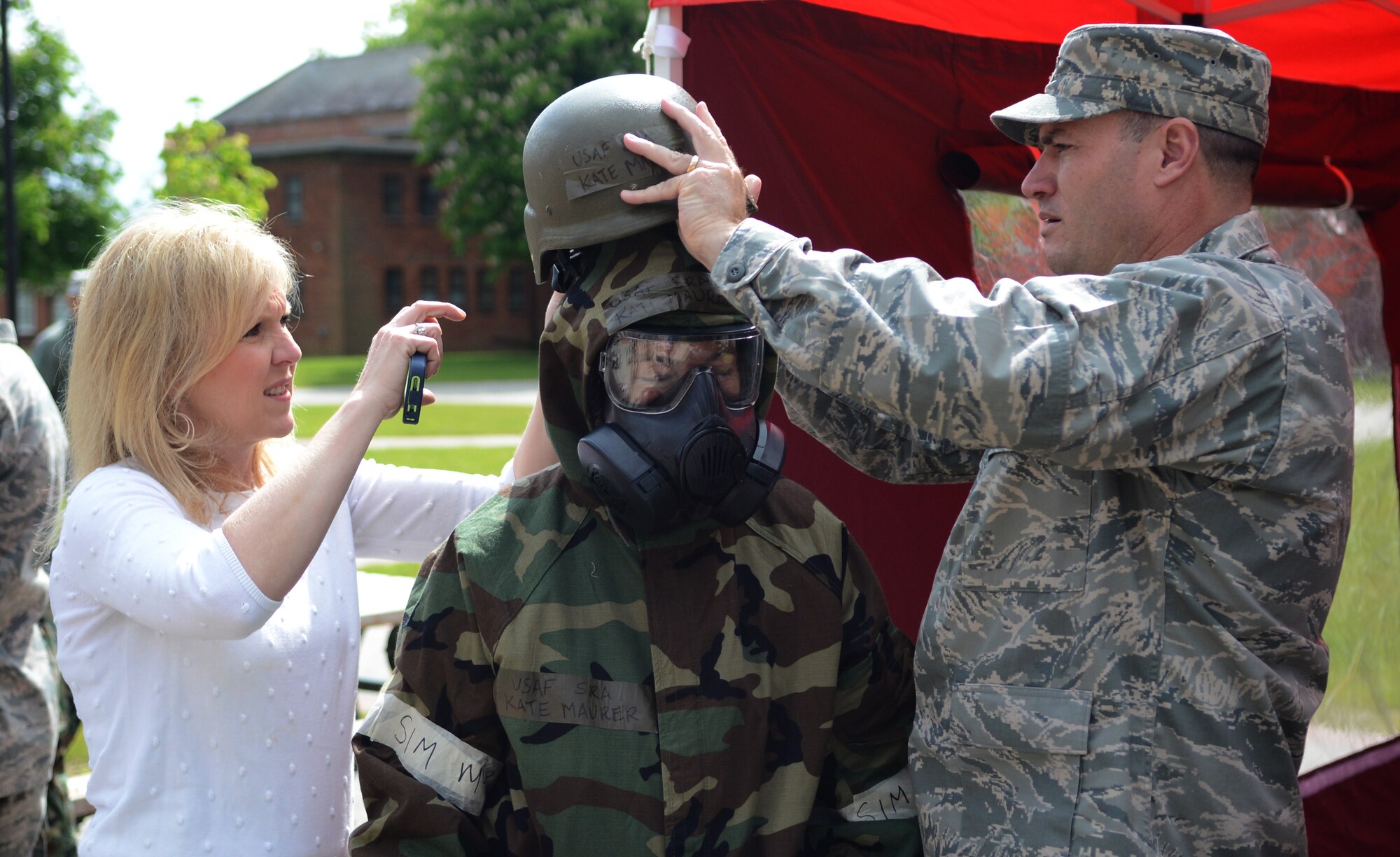 U.S. Air Force Col. Kenneth T. Bibb Jr., left, 100th Air Refueling Wing commander, and his wife Shannon help Georgina Holloway, 100th ARW honorary commander, put on a helmet to complete a set of mission oriented protective posture gear May 13, 2014, during the Honorary Commanders' Day Chip Challenge on RAF Mildenhall, England. The challenge consisted of seven stations, each requiring a team to perform a specific task relating to the mission of RAF Mildenhall. (U.S. Air Force photo by Airman 1st Class Dillon Johnston/Released)