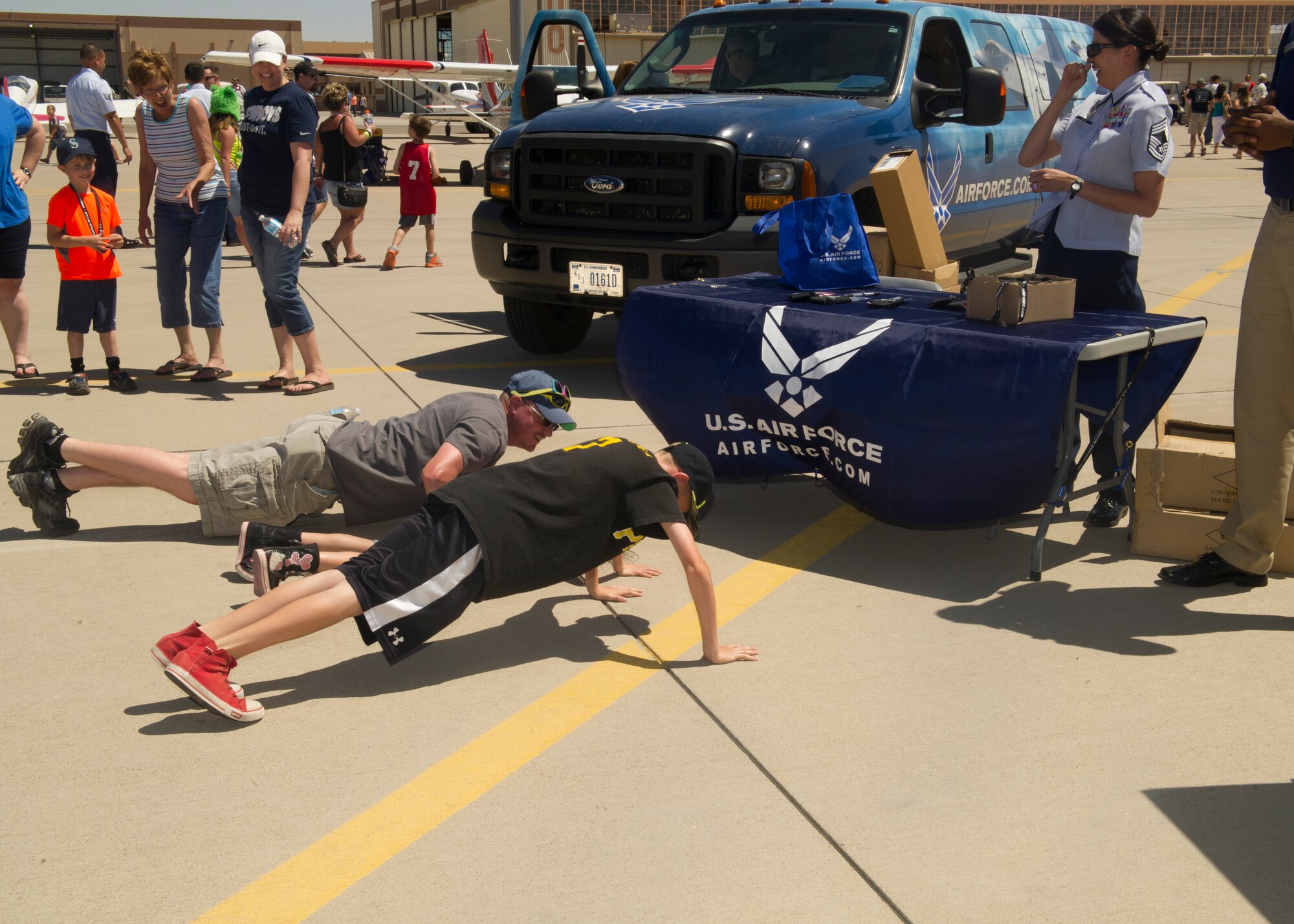 Guests perform pushups at the Air Force recruiting booth during the Open House event at Holloman Air Force Base, N.M., May 10. Team Holloman hosted an Open House showcasing over 50 aircraft and the day-to-day duties of Holloman Airmen. With live flying demonstrations and static displays, thousands of guests attended the event to get a close-up look at the base’s assets and capabilities. Guests were able to view various aircraft, visit numerous vendors, and witness ground demonstrations from squadrons around the base. (U.S. Air Force photo by Airman 1st Class Leah Ferrante/Released) 