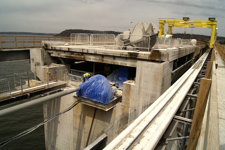 A view of the construction work to replace the 50-year-old Highway 151 Bridge over Keystone Dam. The giant saw referred to as “The Beast” is visible on the bridge deck as it cuts through the concrete. The yellow Gantry Crane, mounted on special rails on the side of the bridge structure, is in the background. Keystone Lake is visible in the foreground where a section of the bridge deck has been removed.                   