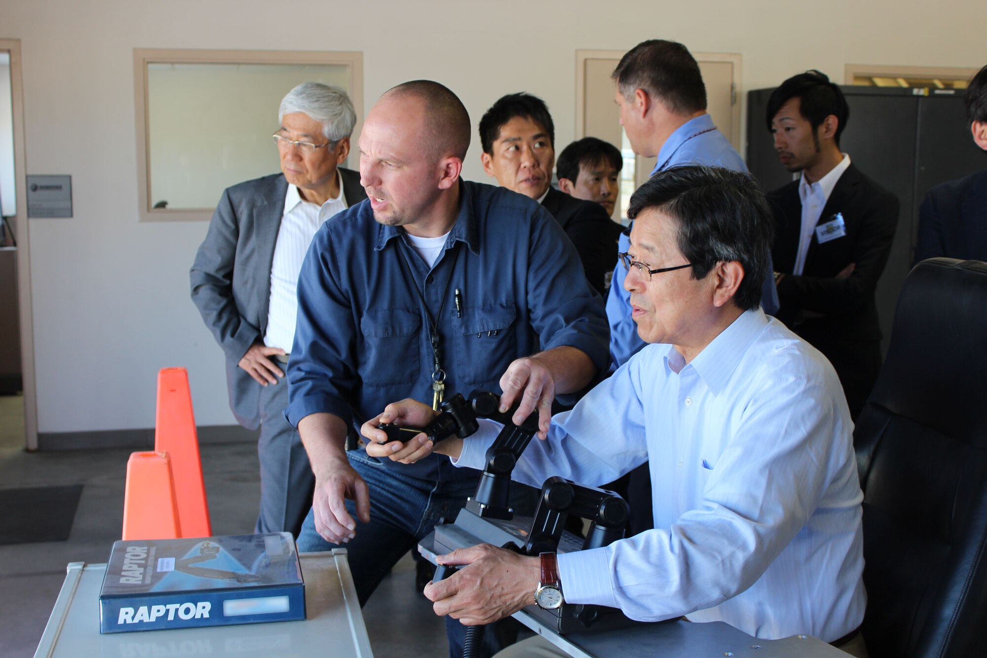Christopher Walsingham (left front), robotics specialist at the Air Force Civil Engineer Center, Det. 1, Tyndall Air Force Base, Fla., explains robotic arm controls to Masao Iwanaga, Chairman of the Defense Technology Research Committee for Unmanned Vehicle Systems. Iwanaga and 17 other members of the Japan Defense Technology Foundation visited AFCEC to see examples of unmanned systems and discuss possible collaboration of robotic technology between the United States and Japan in the future. (U.S. Air Force photo/John Burt)