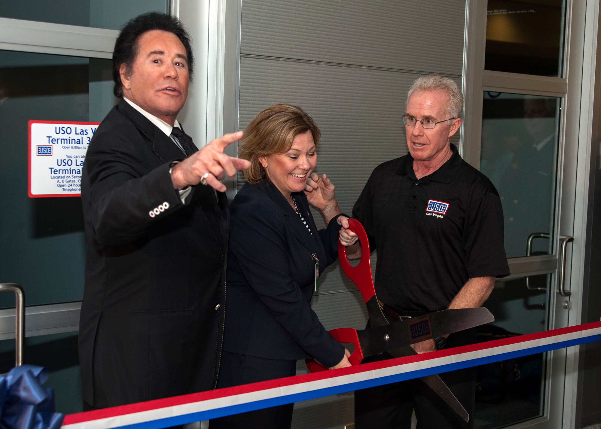 Jennifer Earl, center, USO Las Vegas center director, prepares to cut a ribbon during the grand opening for a new USO lounge at McCarran International Airport’s Terminal 3 May 7, 2014. Celebrity guest Wayne Newton, left, and Jeff Hill, USO regional vice president, were some of more than 100 guests who attended the ceremony.  The USO is a nonprofit, charitable corporation chartered by Congress that relies on donations from individuals, organizations and corporations to support its programs. (U.S. Air Force photo by Tech. Sgt. S.E./Released)