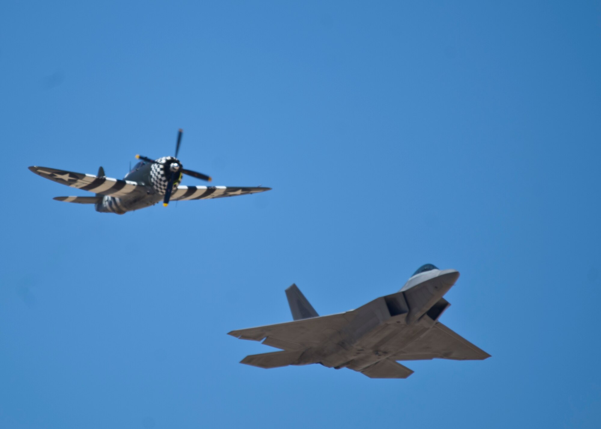 A P-47 Thunderbolt and an F-22 Raptor soar through the skies of the Tularosa Basin during the Open House event at Holloman Air Force Base N.M., May 10. Team Holloman hosted an Open House showcasing over 50 aircraft and the day-to-day duties of Holloman Airmen. With live flying demonstrations and static displays, thousands of guests attended the event to get a close-up look at the base’s assets and capabilities. Guests were able to view various aircraft, visit numerous vendors, and witness ground demonstrations from squadrons around the base. (U.S. Air Force photo by Airman 1st Class Chase Cannon/ Released)