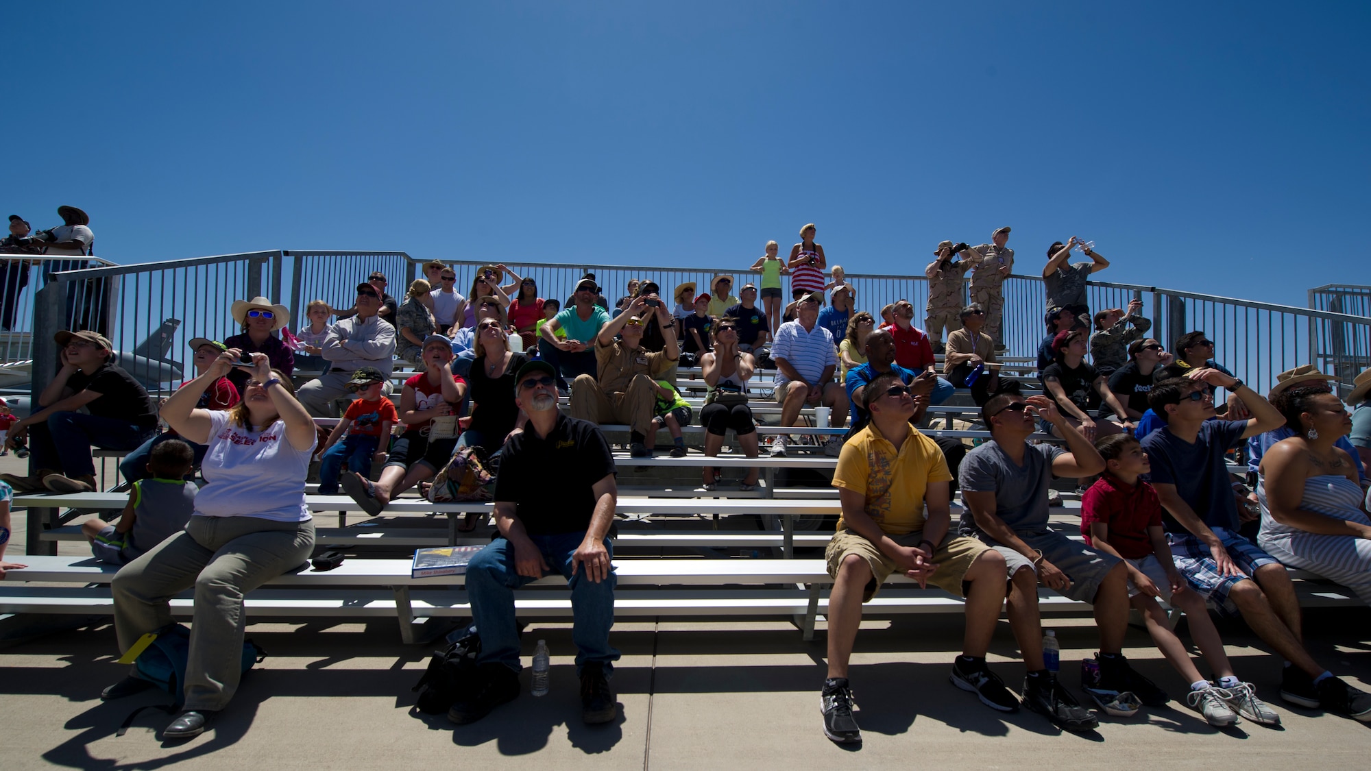 Visitors watch as aircraft fly over the Tularosa Basin during the Open House event at Holloman Air Force Base, N.M., May 10. Team Holloman hosted an Open House showcasing over 50 aircraft and the day-to-day duties of Holloman Airmen. With live flying demonstrations and static displays, thousands of guests attended the event to get a close-up look at the base’s assets and capabilities. Guests were able to view various aircraft, visit numerous vendors, and witness ground demonstrations from squadrons around the base. (U.S. Air Force photo by Airman 1st Class Aaron Montoya / Released)