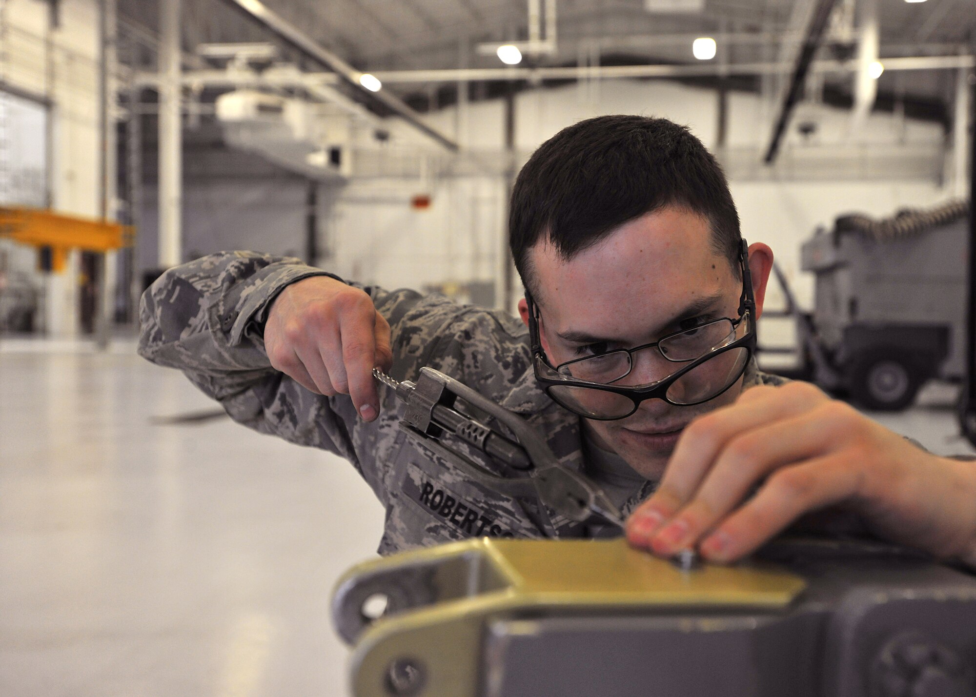 Staff Sgt. Michael Robertson, 69th Maintenance Squadron aerospace ground equipment craftsman, uses safety wire pliers to tighten a cable to a shear bolt on an aircraft tow bar on May 7, 2014, at Grand Forks Air Force Base, N.D. Robertson fixes and inspects equipment when it is near total failure, to be ready for dispatch to the flightline for servicing aircrafts. (U.S. Air Force photo/Senior Airman Xavier Navarro)