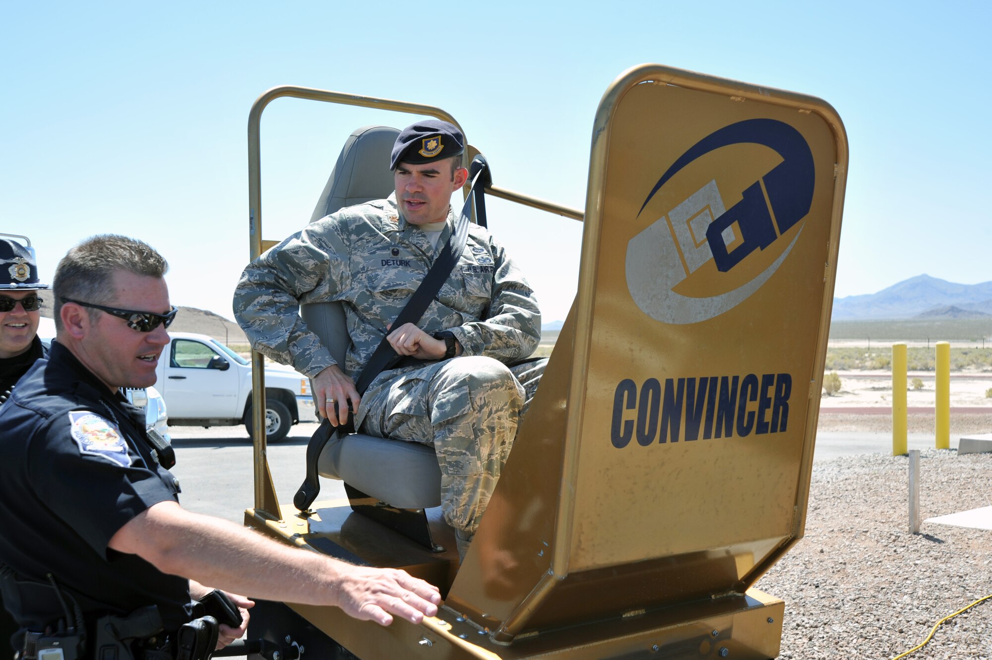 Nevada State Trooper Jeremie Elliott explains the purpose of The Convincer to Maj. Eric Deturk, 799th Security Forces Squadron commander, during an equipment display at Creech Air Force Base as part of Police Week May 14, 2014. The Convincer simulates a 5 mph accident so an individual can feel the safety belt stop their momentum to put into perspective that higher speed accidents will hit harder. (U.S. Air Force photo by Tech. Sgt. S.E./Released)