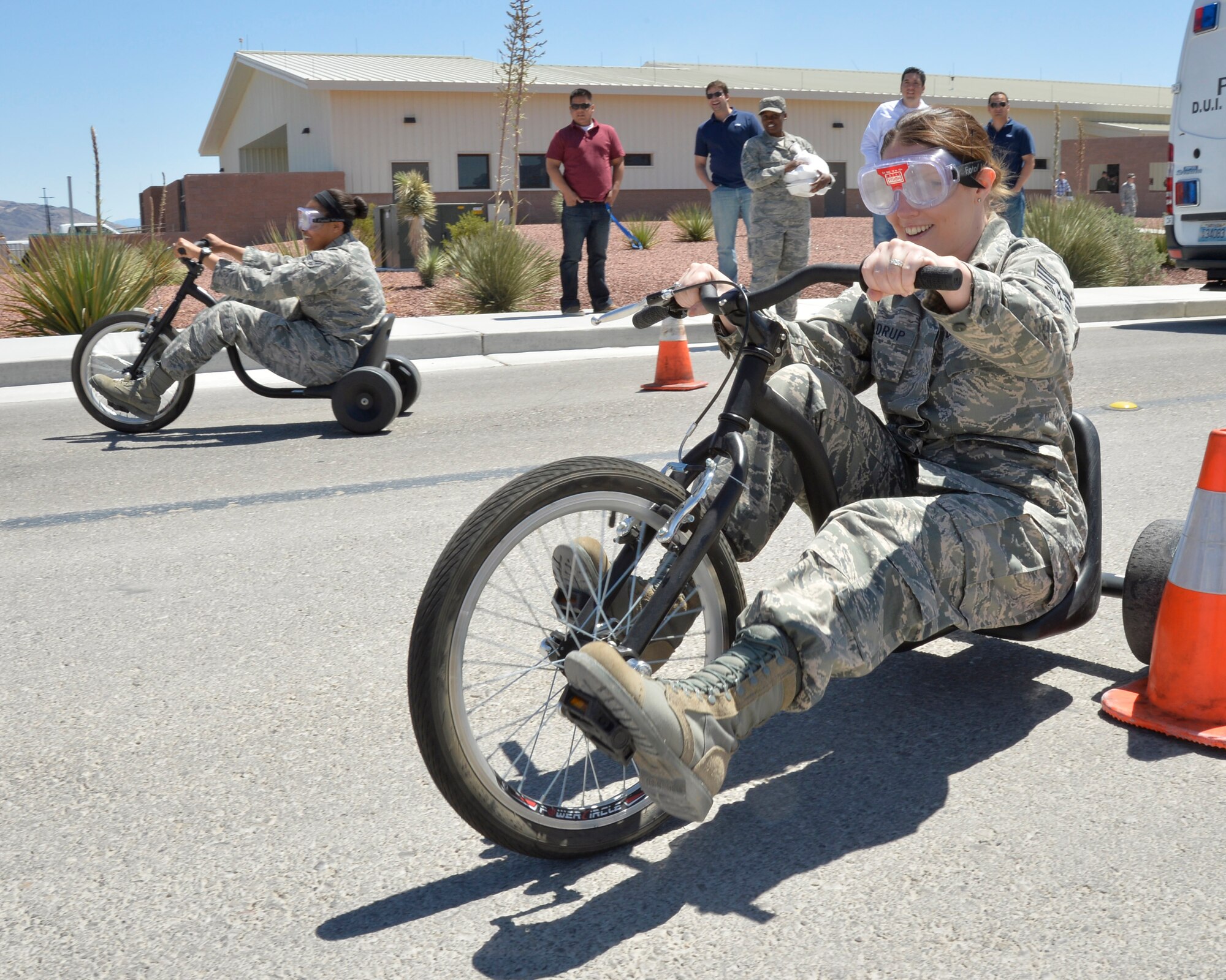 Staff Sgt. Karen, 432nd Operations Support Squadron aviation resource manager, front, and Senior Airman Christy, 432nd OSS command support staff, race through cones on tricycles wearing fatal vision goggles during a demonstration for Police Week May 13, 2014. The fatal vision goggles provided by the Las Vegas Police department are designed to give a person the feeling of what it is like to be intoxicated which makes motor skills more challenging by distorting the vision (Last names have been withheld for security reasons). (U.S. Air Force photo by Staff Sgt. A.K./Released)