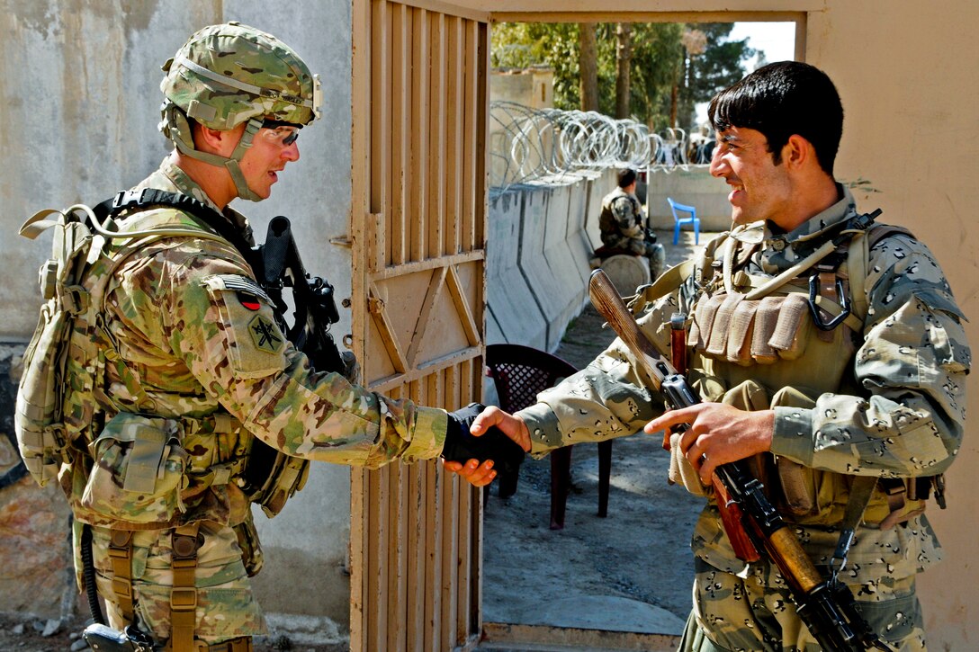 A U.S. soldier, left, and Afghan border policeman exchange greetings after learning they were assigned to the same area to provide security for the first district leaders' shura in Spin Boldak in Kandahar province, Afghanistan, Feb. 11, 2013.  
