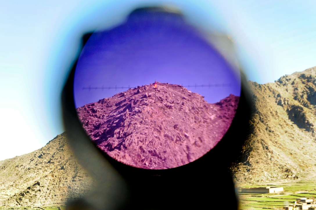 The optic lens on a U.S. soldier's weapon shows view of an old Russian observation point from the Marawara District Center in Kunar province, Afghanistan, Feb. 7, 2013.  
