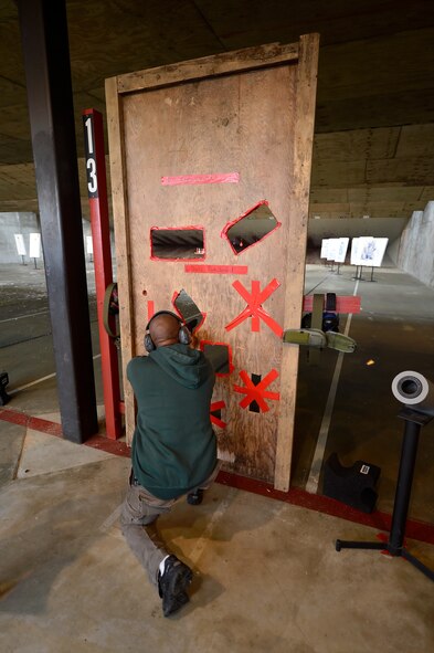 A competitor shoots paper targets from a kneeling position through openings cut in a plywood board May 15, 2014, at Dover Air Force Base, Del. The 436th Security Forces Squadron hosted members of Team Dover along with representatives from local and regional law enforcement agencies for the competition during the 2014 Police Week. (U.S. Air Force photo/Greg L. Davis)