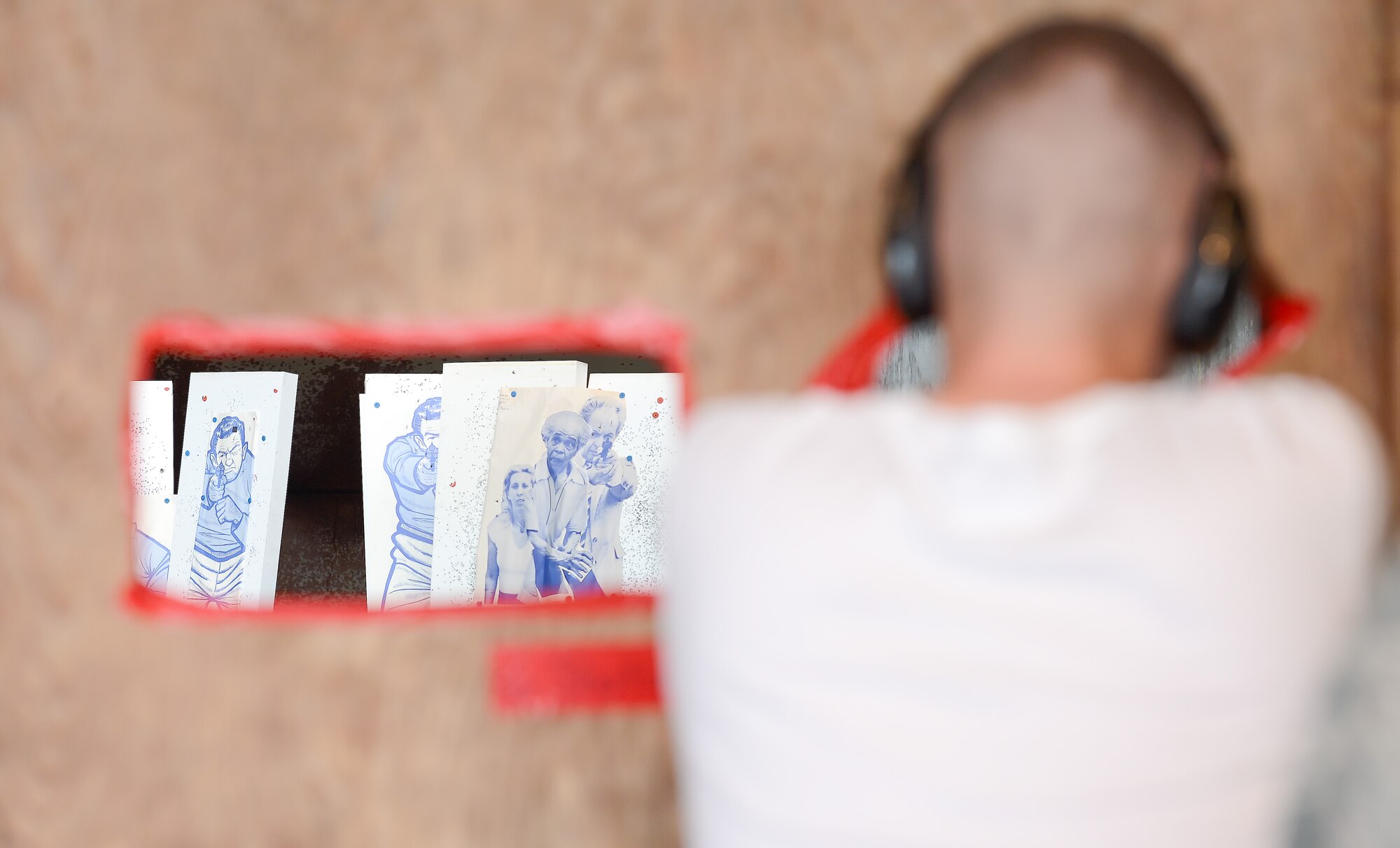 Papers targets portraying combatants and non-combatants can be seen in-focus through a red-framed opening while a shooter takes aim from another opening during a shooting competition May 15, 2014, at the 436th Security Forces Squadron shooting range on Dover Air Force Base, Del. At this station competitors fired one shot from multiple openings cut in to a large plywood board. (U.S. Air Force photo/Greg L. Davis)