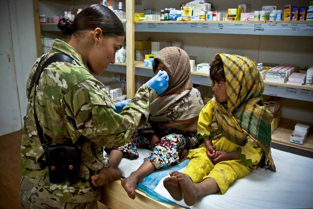 An Afghan girl, right, watches as a U.S. Marine gives her sister cough suppressant in Herat province, Afghanistan, Feb. 14, 2013. Coalition forces held a clinic for women and children in area villages to receive treatment and standard hygiene products.  
