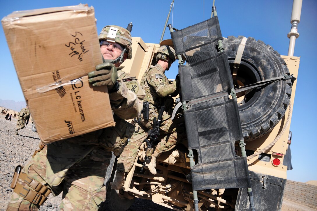 U.S. Army Lt. Col. Mark Martin, left, unloads a box of school supplies during a visit to a local returnee and refugee village in Farah province, Afghanistan, Feb. 9, 2013. Martin, a civil affairs officer, is assigned to Provincial Reconstruction Team Farah.  
