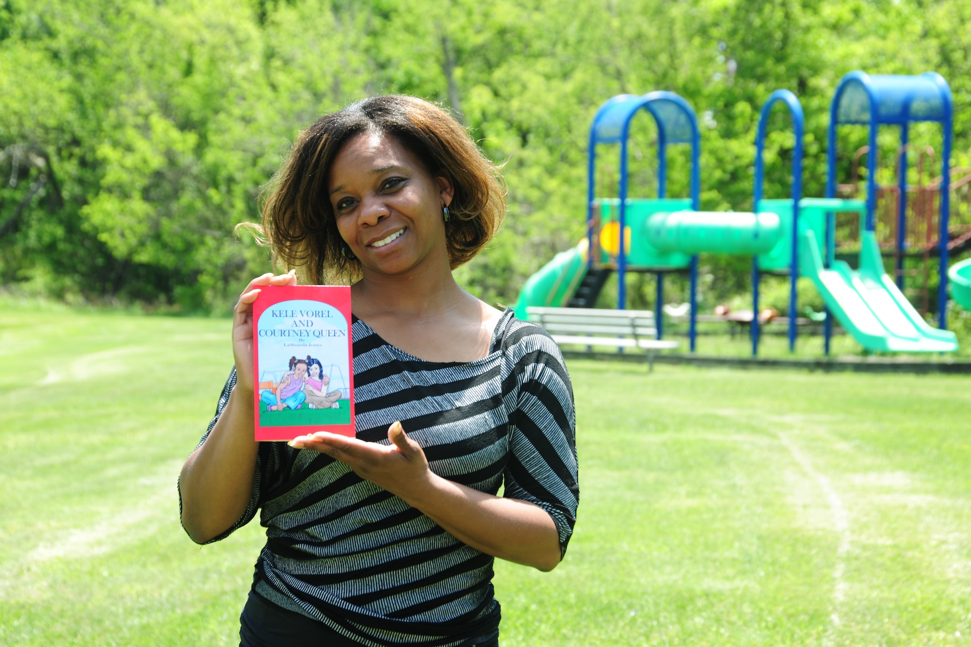LaShanda Jones, holds a copy of her first published childrens' book, "Kele Vorel and Courtney Queen" on May 19, 2014, in front of the Joint Base Andrews, Md.,459th Air Refueling Wing playground. Jones, a retired Air Force veteran, is the chief of finance at the wing. (U.S. Air Force photo / Amber J. Russell)