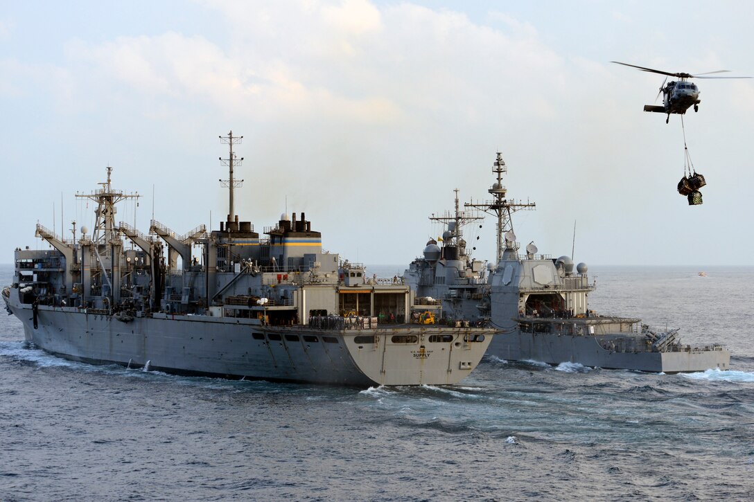 An MH-60S Sea Hawk helicopter carries stores from the flight deck of the Military Sealift Command fast combat support ship USNS Supply to the flight deck of aircraft carrier USS John C. Stennis as the guided-missile cruiser USS Mobile Bay steams alongside during a replenishment at sea in the Arabian Sea, Nov. 24, 2012.  
