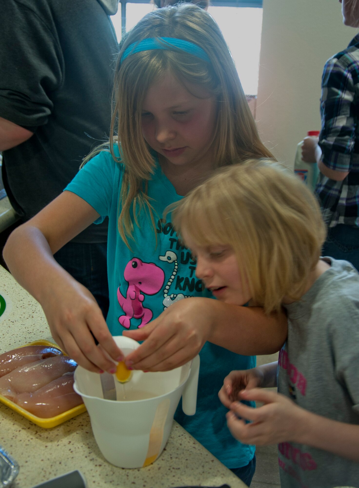 140521-F-GZ967-011 Samantha Chernogorec, 9, daughter of Tech. Sgt. Amanda Chernogorec, 90th Security Forces Squadron, cracks an egg into a dish during a youth center cooking competition in the Fall Hall Community Center May 21 while Emma Hinnershitz, 10, daughter of Master Sgt. Micki Hinnershitz, 90th Medical Operations Squadron, watches on. The two, with the help of their teammates, created a chicken parmesan dish. (U.S. Air Force photo by Airman 1st Class Brandon Valle)