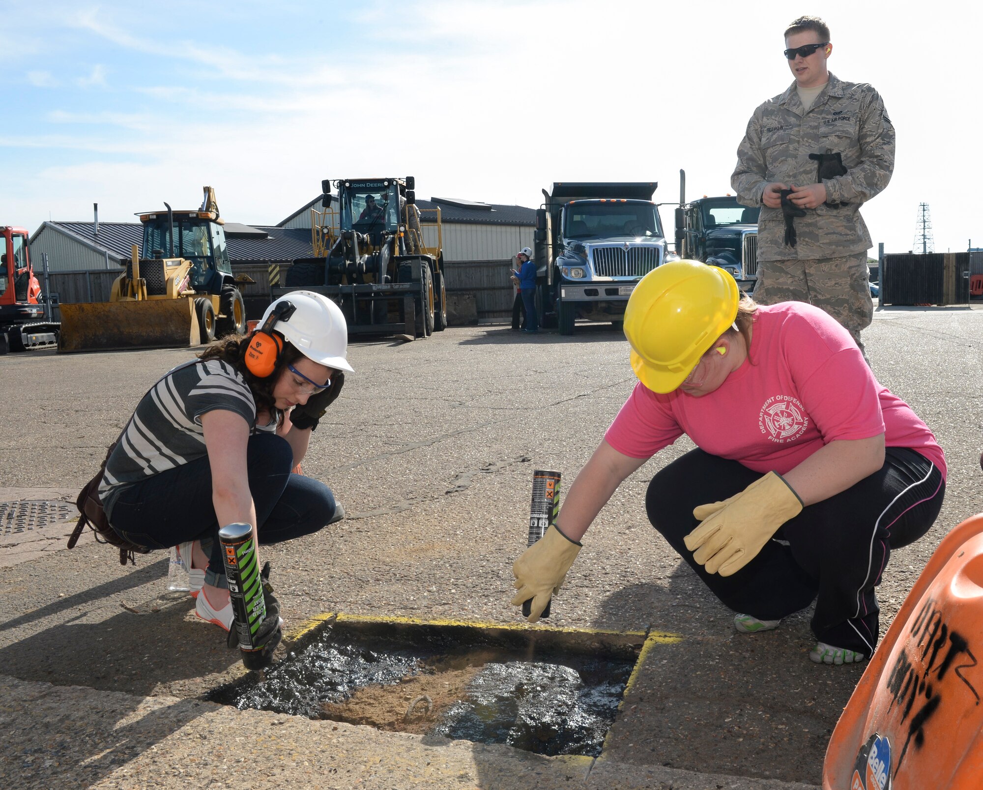 Spouses cover a hole with tac coat during Take Your Spouse to Work Day on Royal Air Force Lakenheath, England, May 21, 2014. Tac coat is used during road repairs to seal dirt in place before doing further maintainace. (U.S. Air Force photo by Airman 1st Class Nigel Sandridge/Released)