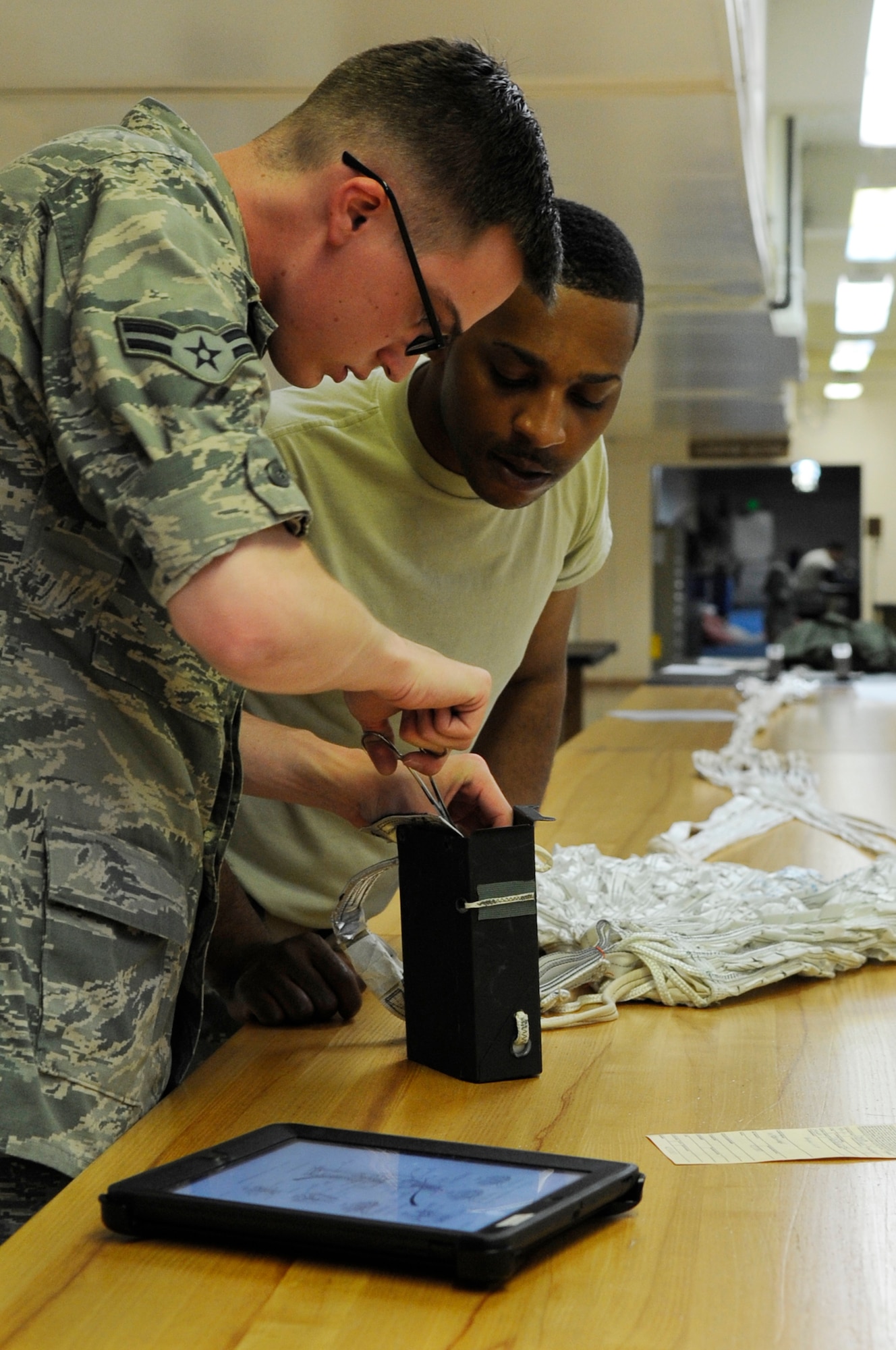 U.S. Air Force Airman 1st Class Stephen Carter, 18th Operations Support Squadron aircrew flight equipment packs a drogue parachute while Staff Sgt. Marques Bones, 18th OSS aircrew flight equipment specialist inspects his work on Kadena Air Base, Japan, May 21, 2014. Each parachute goes through up to seven in-process inspections, as well as a final quality control inspection to maintain safety standards. (U.S. Air Force photo by Senior Airman Marcus Morris)