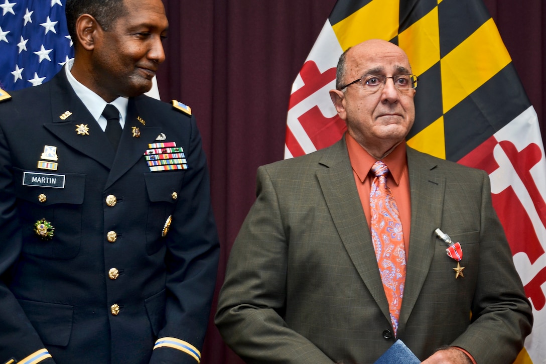 Defense Information School Commandant Army Col. Jeremy Martin, commandant of Defense Information School, looks on at former Army Spc. 4 Charles Shyab, a Vietnam War veteran, after he received a Bronze Star with valor medal during a ceremony at the school on Fort Meade, Nov. 9, 2012.  
