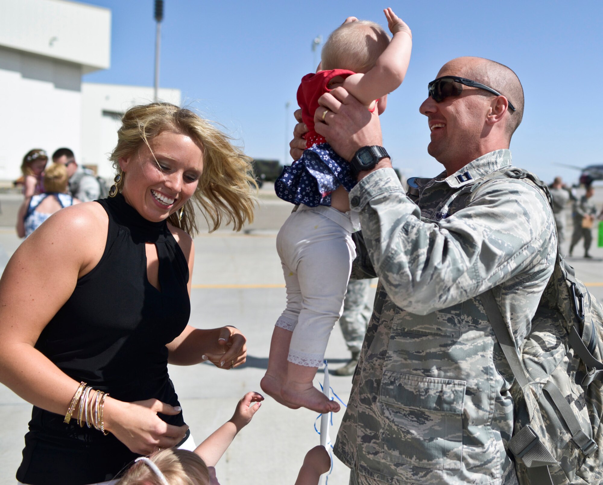 A 726th Air Control Squadron captain holds his young daughter as his wife and other daughter look on, immediately after returning from deployment to Afghanistan May 23, 2014. 'Hardrock' Airmen provided time critical battle management command and control using sensors and communication located across Afghanistan. (U.S. Air Force photo by Master Sgt. Kevin Wallace/RELEASED)