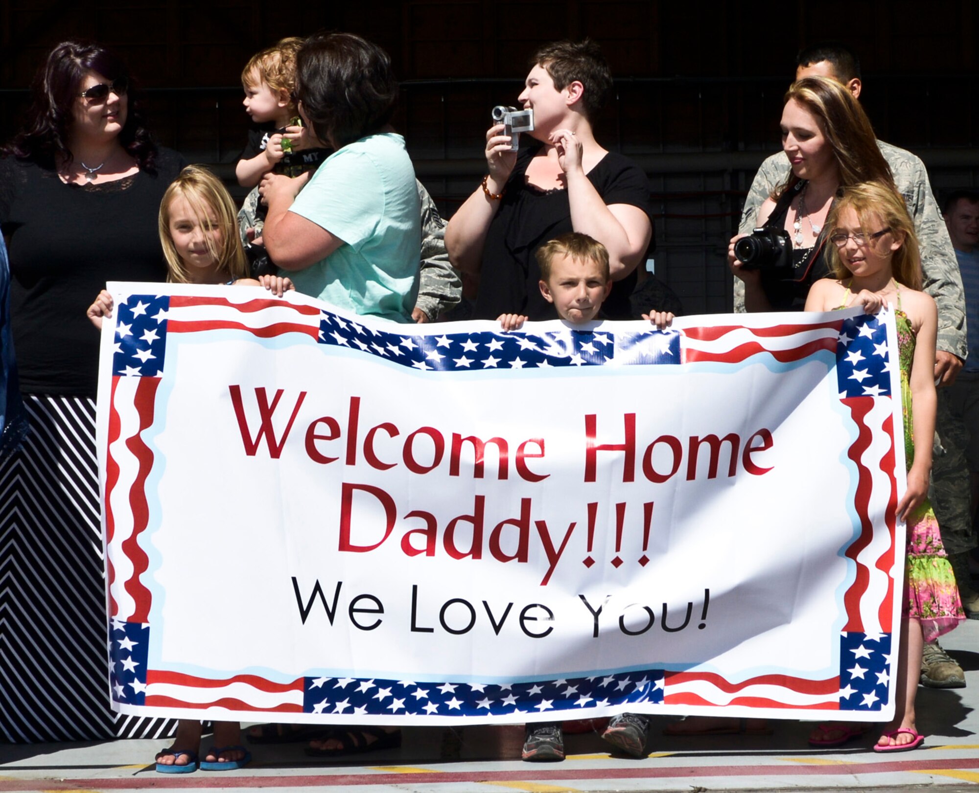 Family members hold a ‘Welcome Home Daddy!’ banner and wait anxiously as the 726th Air Control Squadron returns from deployment to various locations in Afghanistan and Southwest Asia and were reunited with family and friends at a celebration at the Mountain Home Air Force Base flightline, May 23, 2014, at the base in Southwestern Idaho. 'Hardrock' Airmen provided time critical battle management command and control using sensors and communication located across Afghanistan. (U.S. Air Force photo by Master Sgt. Kevin Wallace/RELEASED)