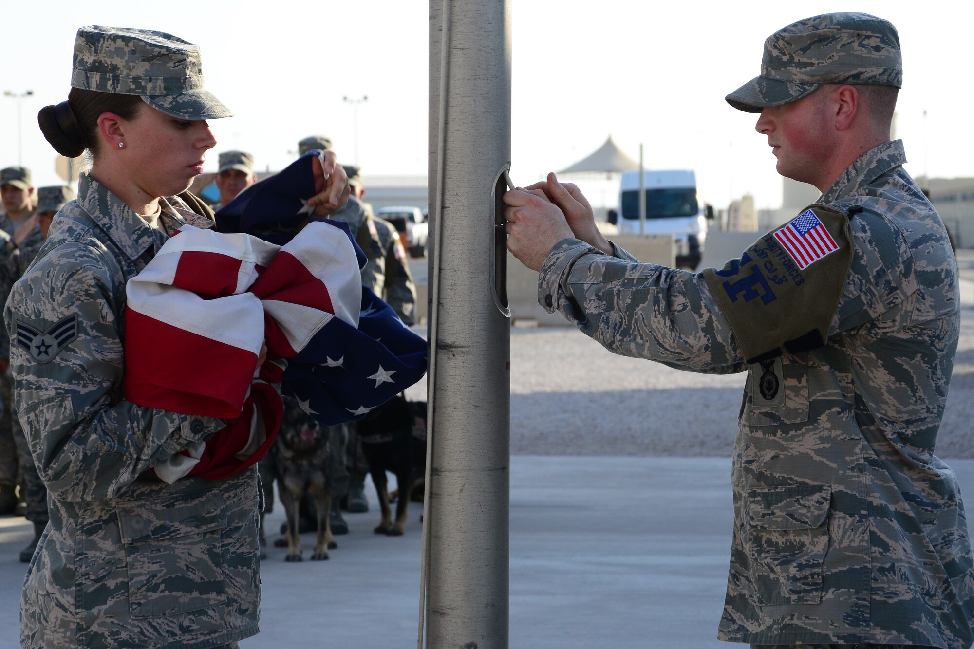 U.S. Air Force Senior Airman Andrea Brunsvold, left, and Airman 1st Class Tienton Winters retrieve the flag during a retreat ceremony at Al Udeid Air Base, Qatar, May 16, 2014.  Brunsvold is deployed from Peterson Air Force Base and hails from Sidney, Montana.  Winters is deployed from Tinker Air Force Base and hails from Roy, Utah.  The ceremony was held as part of National Police Week to pay respect for all fallen service members.  (U.S. Air Force Photo by Master Sgt. Marcelo Joniaux)   