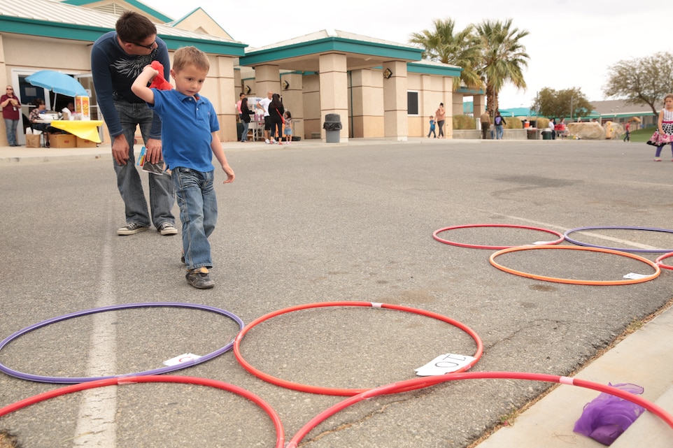 Alexander Freeman, 4, son of Staff Sgt. Richard Freeman, Marine Corps Communication-Electronics School, throws a bean bag into a Hula-Hoop target as his father watches over him during the Month of the Military Child Carnival hosted by the Child Development Center, April 4, 2014.