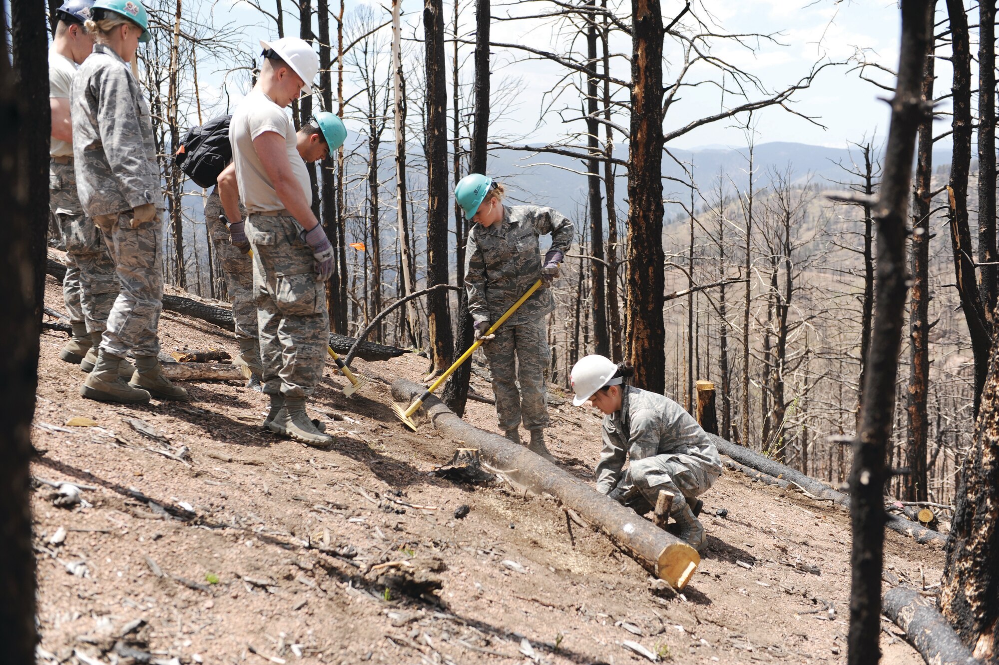 Cadet 1st Class Whitney Briggs (middle), an Academy cheerleader, joins Falcon Football players and other cheerleaders to turn a log barrier into a mini-earthen dam to control flash-flooding and erosion on the Waldo Canyon Burn Scar Tuesday in Wellington Gulch. (John Van Winkle/U.S. Air Force photo)