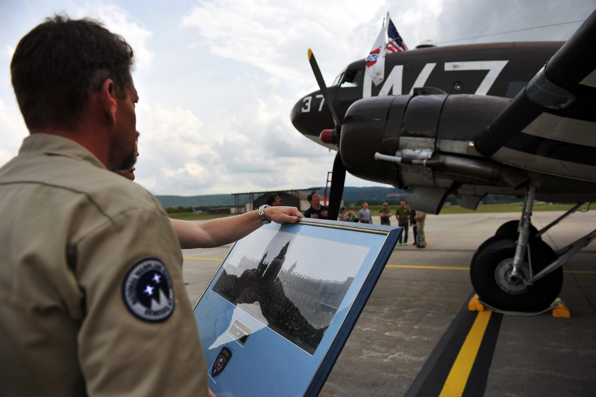 A pilot from the 37th Airlift Squadron holds a group photo from 1944 of the 37th Troop Carrier Squadron taken in front of the same Douglas C-47 Skytrain, designated Whiskey 7, just after landing the aircraft at Ramstein Air Base, May 26, 2014. Whiskey 7 was the lead carrier of 37th Troop Carrier Squadron that took part in dropping the 82nd Airborne Division near St. Mere Eglise, France during D-Day, June 6th, 1944. The historical aircraft landed in Ramstein before heading to Normandy to take part in commemoration events for the 70th Anniversary of D-Day. (U.S. Air Force photo/Staff Sgt. Sara Keller)