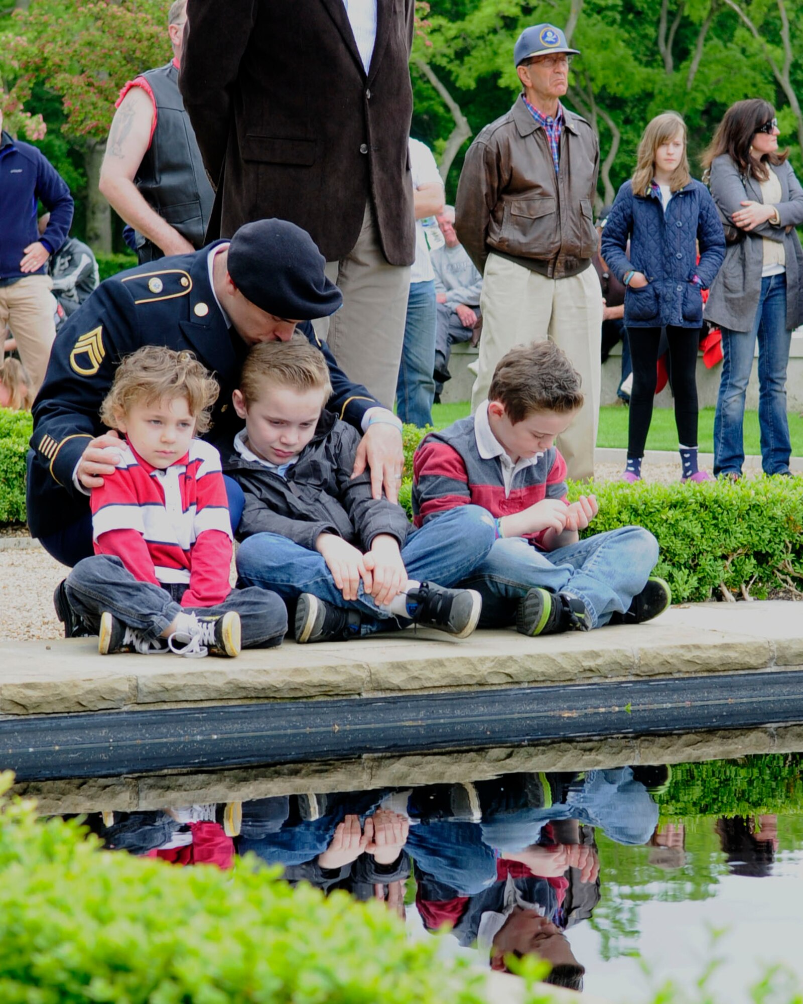 U.S. Army Staff Sgt. James Marinelli, Defense Intelligence Agency, Joint Analysis Center, RAF Molesworth from Lancaster, Calif., kisses his sons, Cole, center, 7; Carson, left, 5; and Jakob, 8, as they reflect on Memorial Day May 26, 2014, at the Madingley American Cemetery in Cambridge, England. Memorial Day is an annual tradition honoring fallen service members. (U.S. Air Force photo by Karen Abeyasekere/Released)