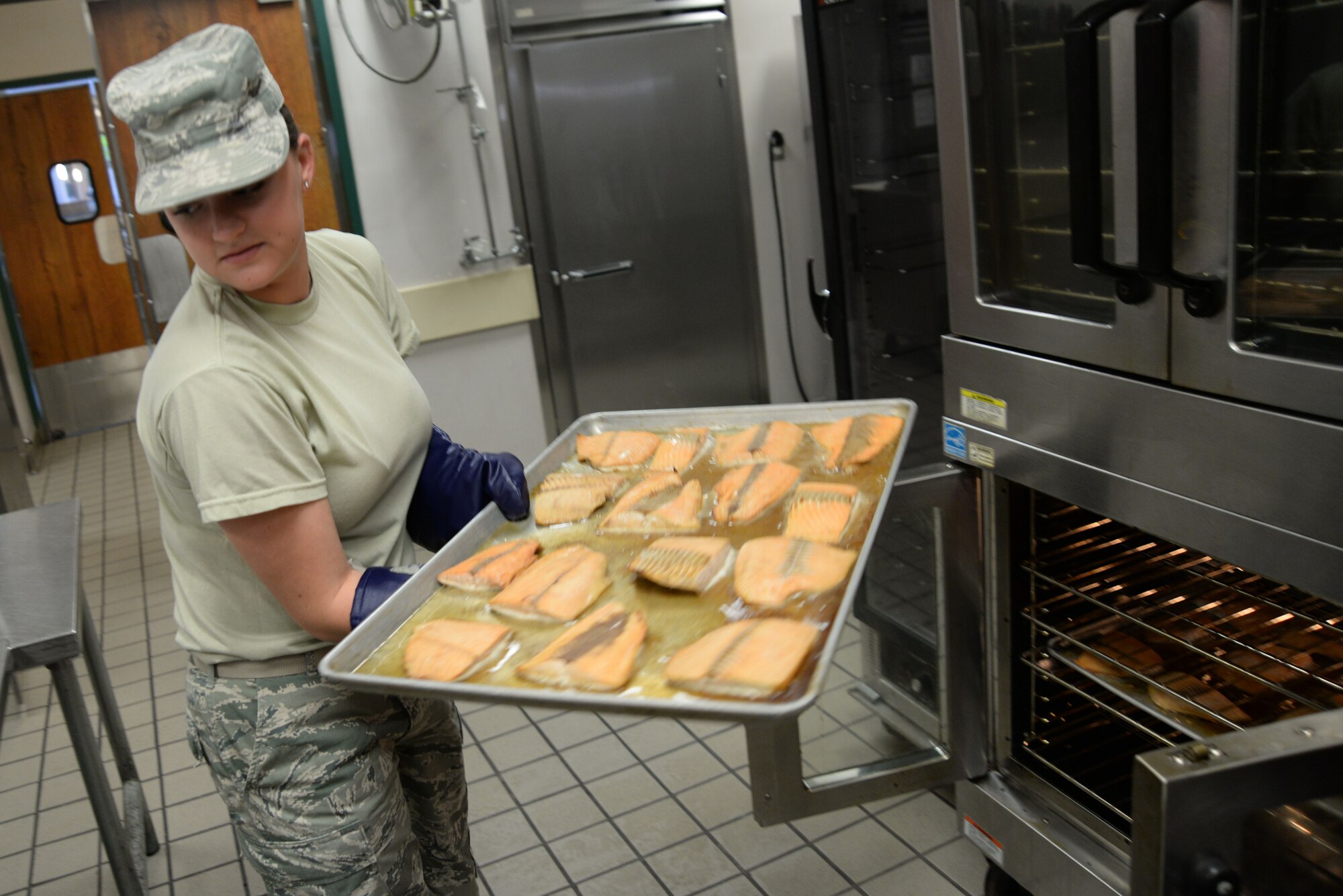 U.S. Air Force Airman 1st Class Emma Makransky, 20th Force Support Squadron food service specialist, takes a tray of fish out of the oven at the Chief Master Sgt. Emerson E. William Dining Facility, May 21, 2014, Shaw Air Force Base, S.C. Airmen have to begin preparation for the next meal service up to two hours in advance. (U.S. Air Force photo by Airman 1st Class Michael A. Cossaboom/Released)