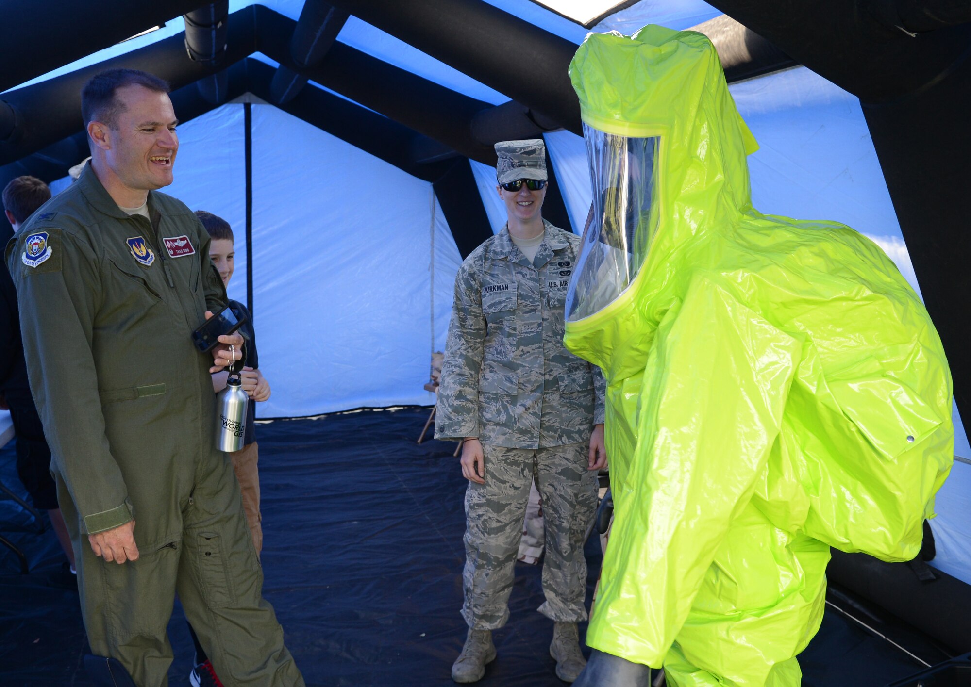U.S. Air Force Col. Kenneth T. Bibb Jr., left, 100th Air Refueling Wing commander, watches as his son, Logan, tries on a protective suit May 23, 2014, during the Team Mildenhall job shadow day on RAF Mildenhall, England. Each of the squadrons on base set up displays and events for children to experience. (U.S. Air Force photo by Airman 1st Class Dillon Johnston/Released)