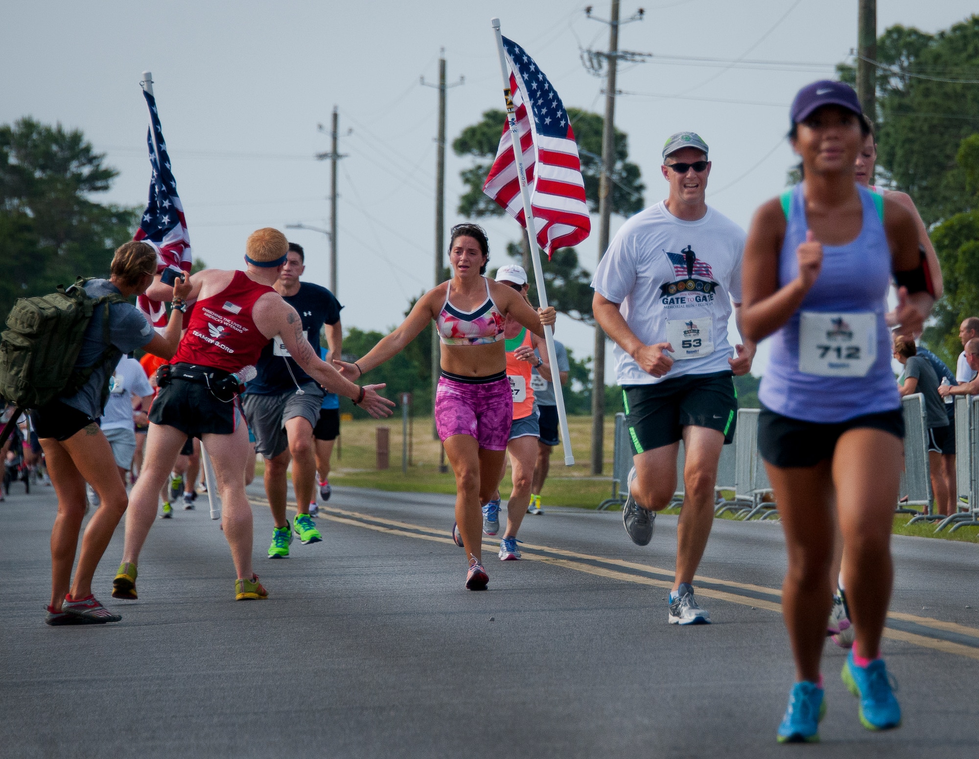 A female runner carrying a flag is cheered on as she approaches the finish line of the 29th annual Gate-to-Gate Run May 24 at Eglin Air Force Base, Fla. More than 1,200 people participated in the 4.4-mile race. Many of the runners paid their respects by dropping off flowers in front of the All Veterans Memorial as they raced by. (U.S. Air Force photo/Samuel King Jr.)
