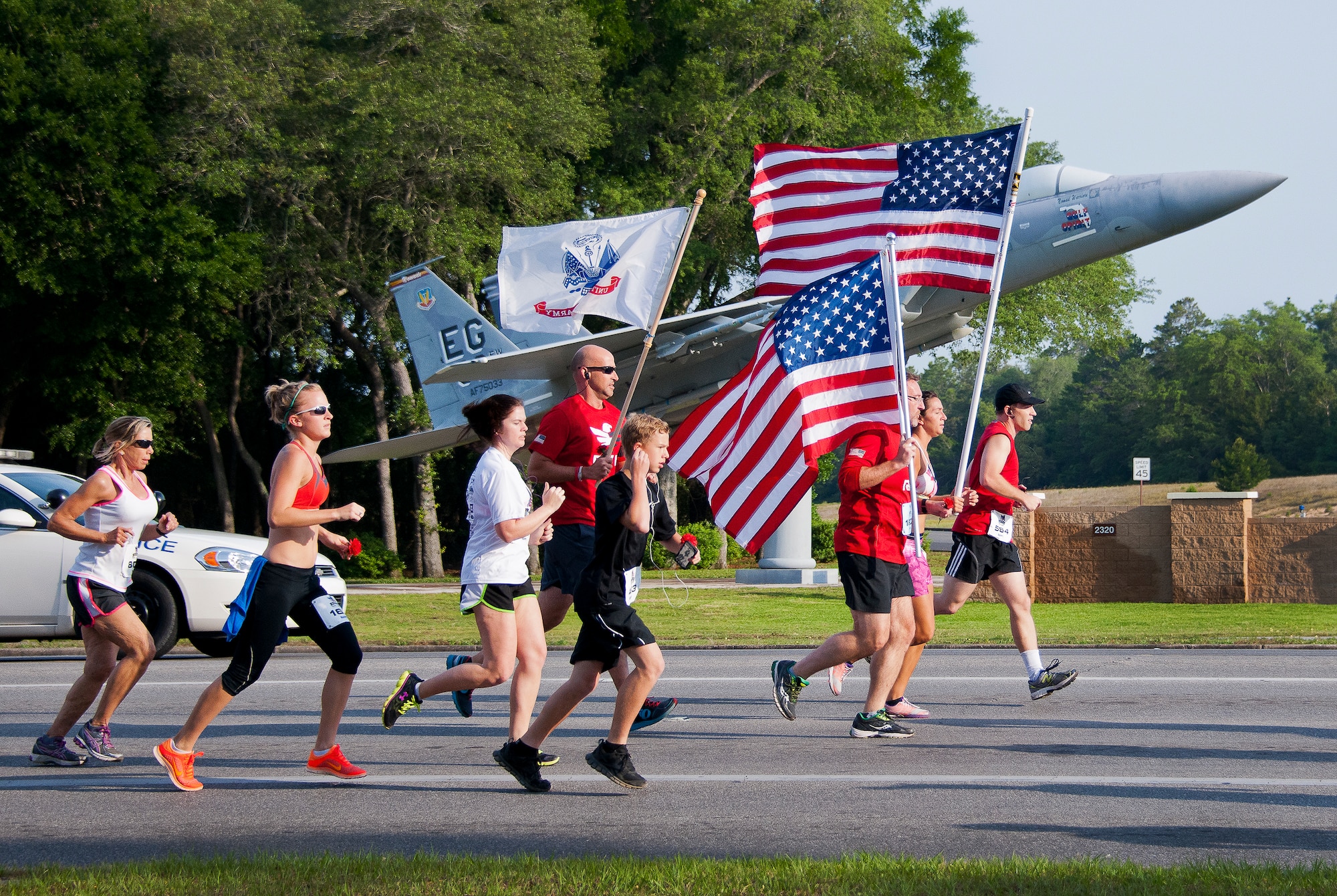 A group of runners carry flags as they pass the F-15 static display at the 29th annual Gate-to-Gate Run May 24 at Eglin Air Force Base, Fla. More than 1,200 people participated in the 4.4-mile race. Many of the runners paid their respects by dropping off flowers in front of the All Veterans Memorial as they raced by. (U.S. Air Force photo/Samuel King Jr.)