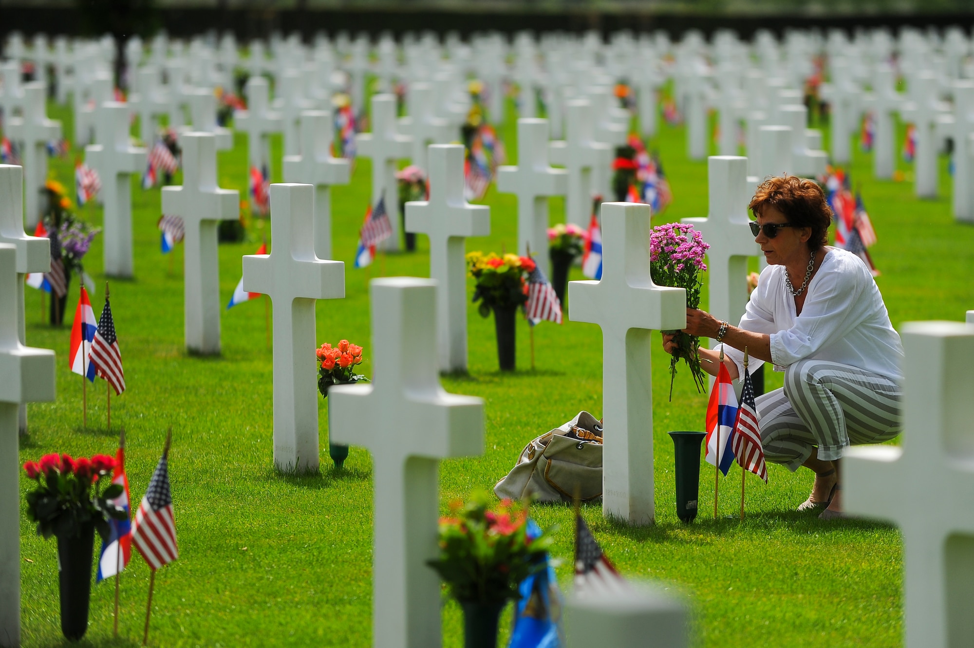 A spectator plants flowers on a headstone at the Netherlands American Cemetery prior to the start of a Memorial Day ceremony May 25, 2014, Margraten, Netherlands. Dutch families can adopt a gravesite and maintain it as a way of showing respect for the actions of the fallen service member. (U.S. Air Force photo by Senior Airman Rusty Frank/Released)