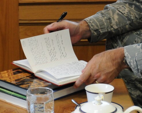 U.S. Air Force Col. Kenneth T. Bibb Jr., 100th Air Refueling Wing commander, writes in a book belonging to Joe Urice, a World War II veteran, during a base visit May 22, 2014, on RAF Mildenhall, England. Urice served from December 1944 to November 1945 with the 100th Bombardment Group as a B-17 Flying Fortress tail-gunner. During his visit, Urice asked people he met to write a message in his book. (U.S. Air Force photo by Gina Randall/Released) 