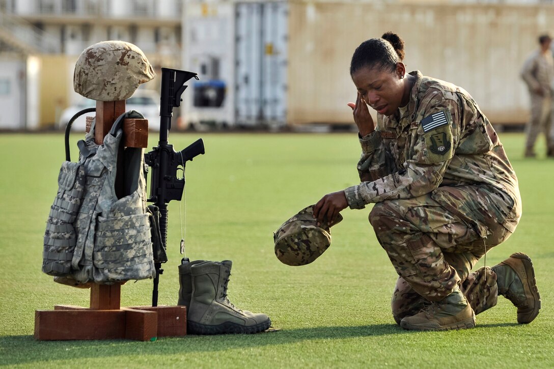 U.S. Air Force Master Sgt. Tiffany Robinson kneels in front of a battlefield cross following a Memorial Day ceremony on Camp Lemonnier, Djibouti, May 26, 2014. Robinson is assigned to 449th Air Expeditionary Group. The cross was created with combat gear representing each of the five U.S. military branches in commemoration of fallen service members.