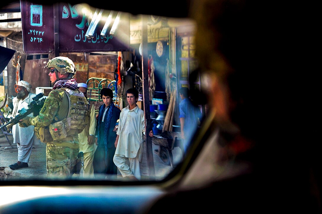 U.S. Army Staff Sgt. James Bates pulls security as Afghans look on during a mission to visit an official in Farah City in Afghanistan's Farah province, Sept. 25, 2012. Bates is assigned to Provincial Reconstruction Team Farah.  

