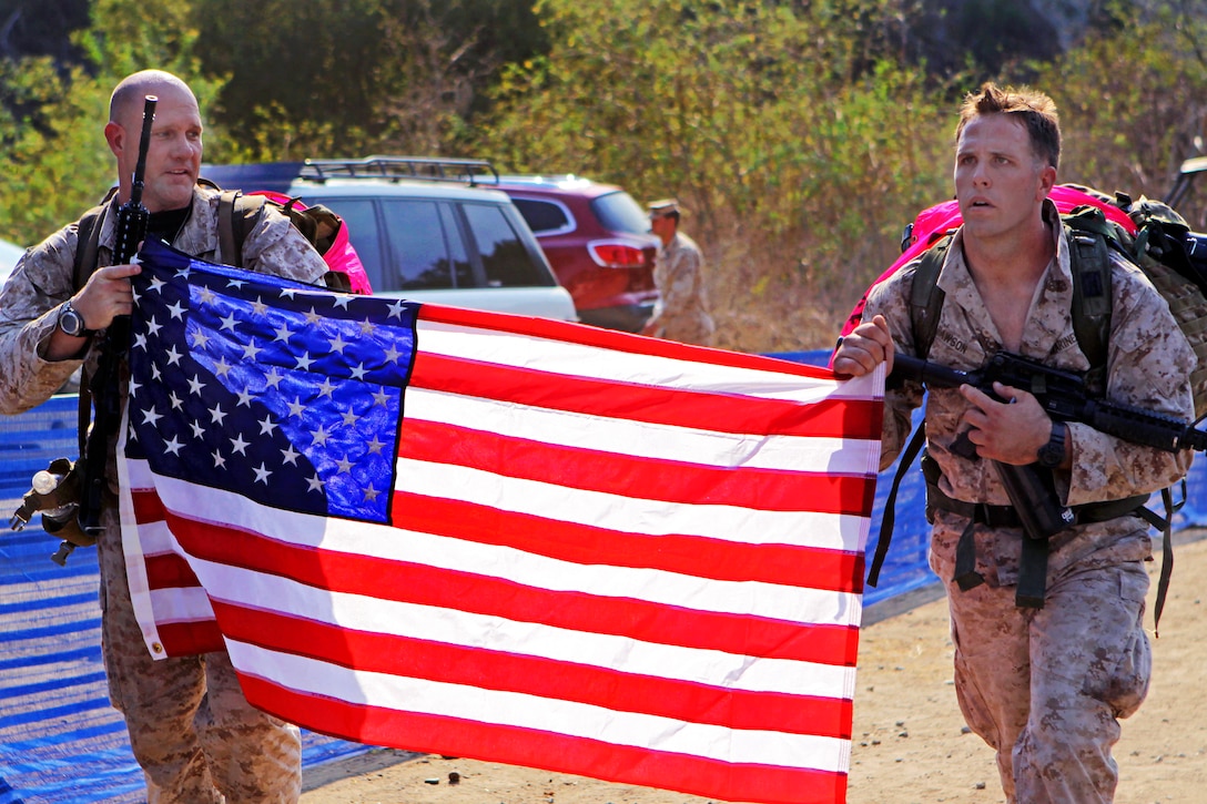 Marine Corps Master Sgt. Christopher May, left, and Marine Corps Sgt. Mark Rawson carry an American flag to honor the Recon Marines who were killed during Operation Iraqi Freedom and Operation Enduring Freedom on their way to drag a 250-pound Zodiac raft across the finish line of the 4th Annual Recon Challenge on Marine Corps Base Camp Pendleton, Calif., Sept. 15, 2012.  
