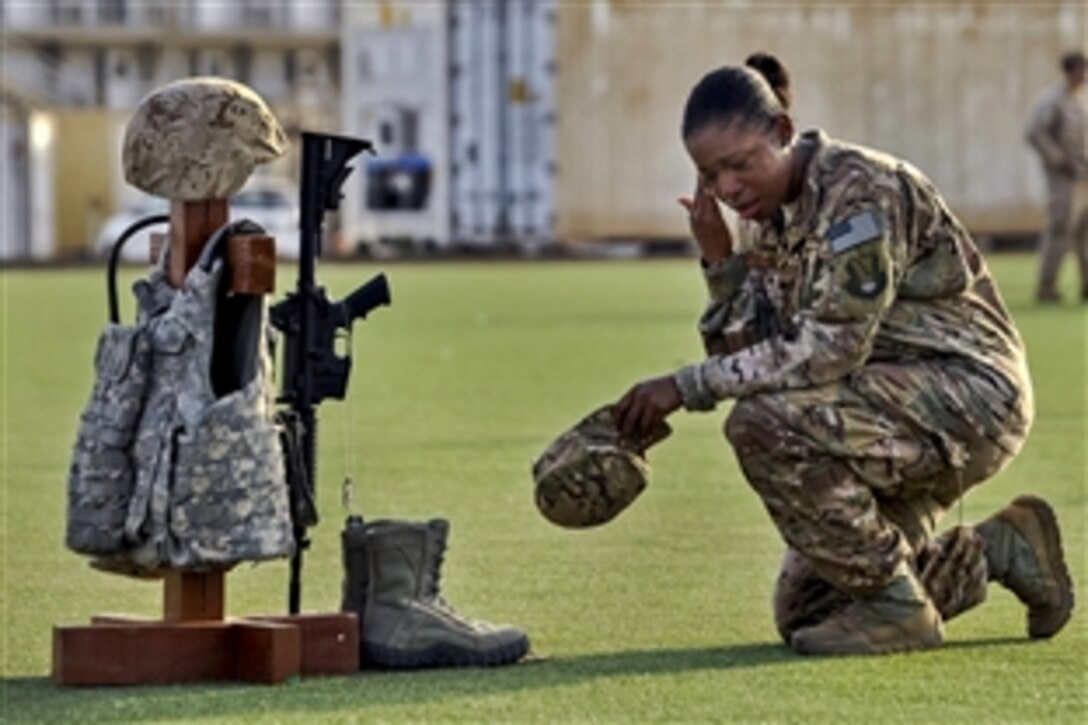 U.S. Air Force Master Sgt. Tiffany Robinson kneels in front of a battlefield cross following a Memorial Day ceremony on Camp Lemonnier, Djibouti, May 26, 2014. Robinson is assigned to 449th Air Expeditionary Group. Combat gear hangs on the cross to represent each of the five U.S. military branches to commemorate fallen service members. 