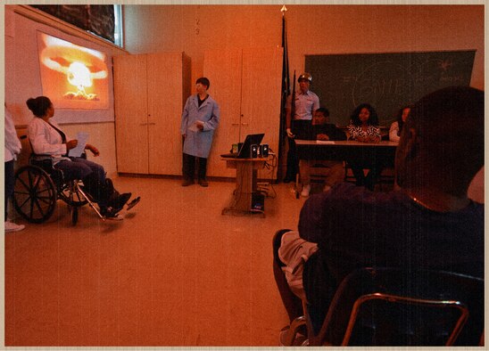 Graphically enhanced photo of Desert Junior-Senior High School students re-enacting the Manhattan Project brief given to President Harry Truman in which scientists explain the first atomic bomb during a "Night at the Museum" event hosted by the students and faculty of Desert Junior Senior High School May 21, 2014. The second annual event was an end-of-year, school-wide project where students transformed the halls of the high school into static displays, living statues and interactive history exhibits. (U.S. Air Force graphic by Jet Fabara)