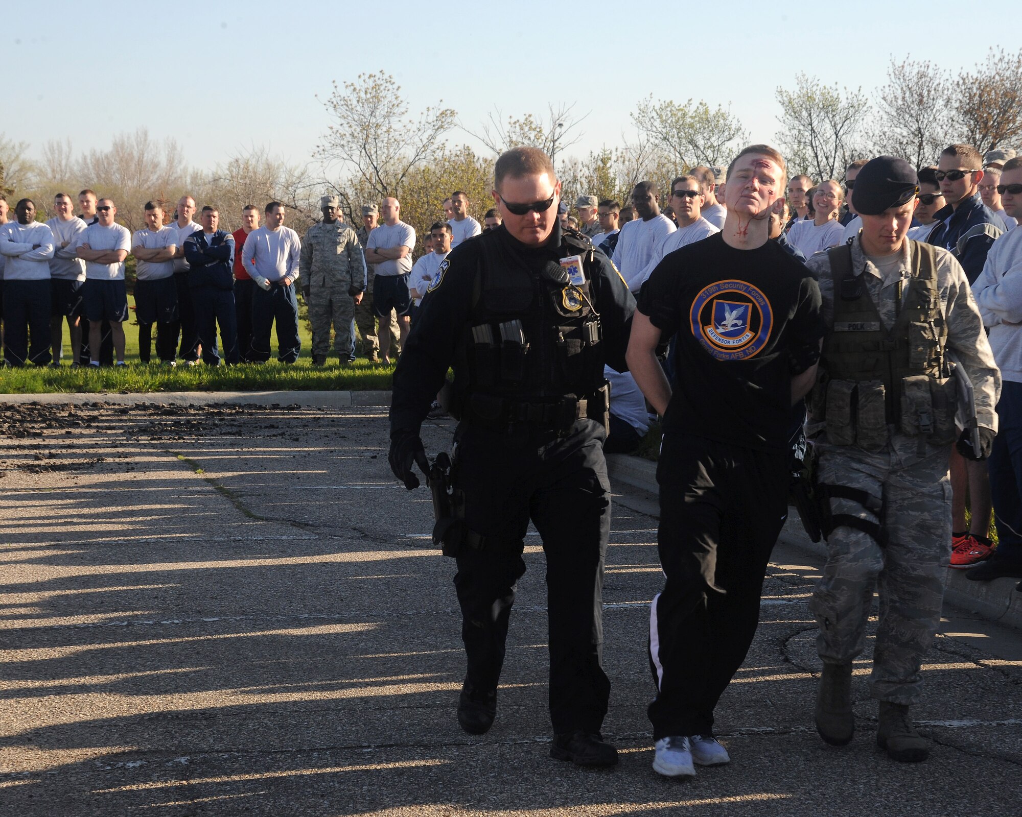 (From left) Robert Hadley and Senior Airman Jedidiah Polk, from the 319th Security Forces Squadron, simulate escorting Senior Airman Caleb Green, 319th Security Forces Squadron desk sergeant,  to jail, who volunteered to play the role of an irresponsible driver during  a simulated vehicle crash caused by someone driving under the influence for Wingman Day held on May 22, 2014, on Grand Forks Air Force Base, N.D. The Wingman Day simulations and demos were a combined effort by multiple base agencies, who intended to provide the most realistic representation of the negative impacts DUI incidents can have not only on the driver, but multiple people. (U.S. Air Force photo/Senior Airman Zachiah Roberson)