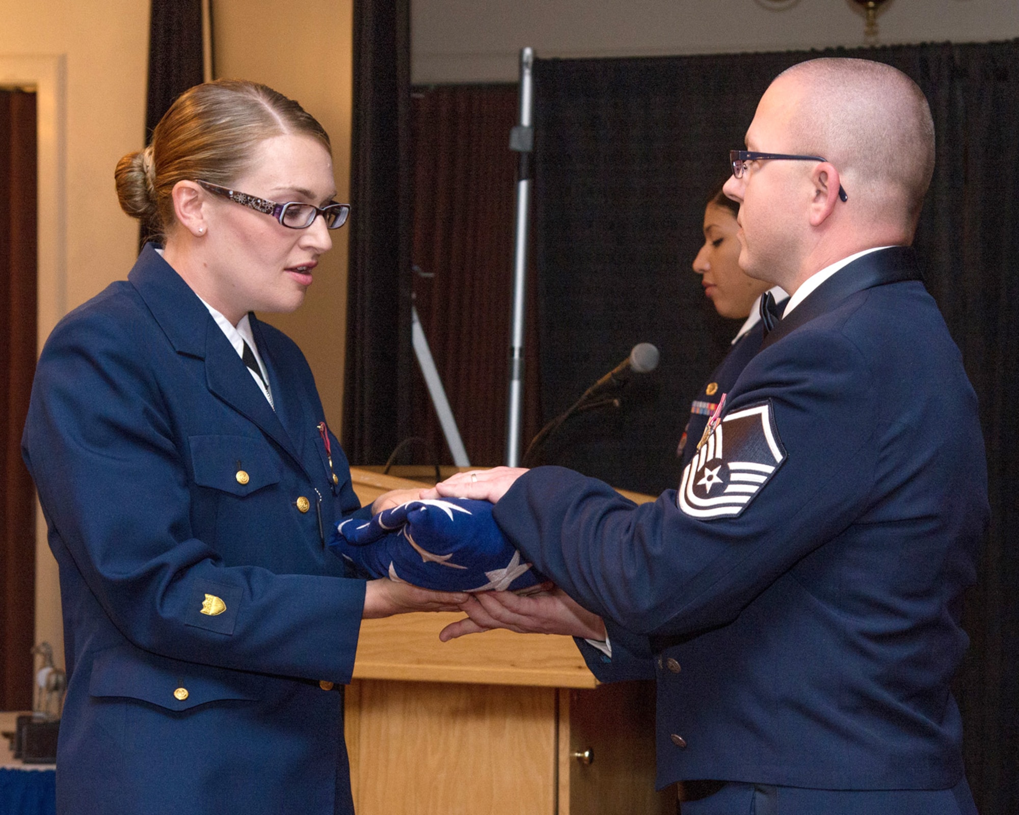 HANSCOM AIR FORCE BASE, Mass. – Petty Officer 3rd Class Jessica Olmeda (left), U.S. Coast Guard Sector Boston, presents a flag to Master Sgt. Charles R. Humphrey Jr., Airman Leadership School superintendent, during a 14D class presentation during the ALS graduation ceremony at the Minuteman Commons May 22. Olmeda was awarded the ALS John L. Levitow award, also known as the Most Distinguished Graduate, for achieving the highest summative objective and performance evaluations as well as instructor and peer leadership points. (U.S. Air Force photo by Walter Santos)