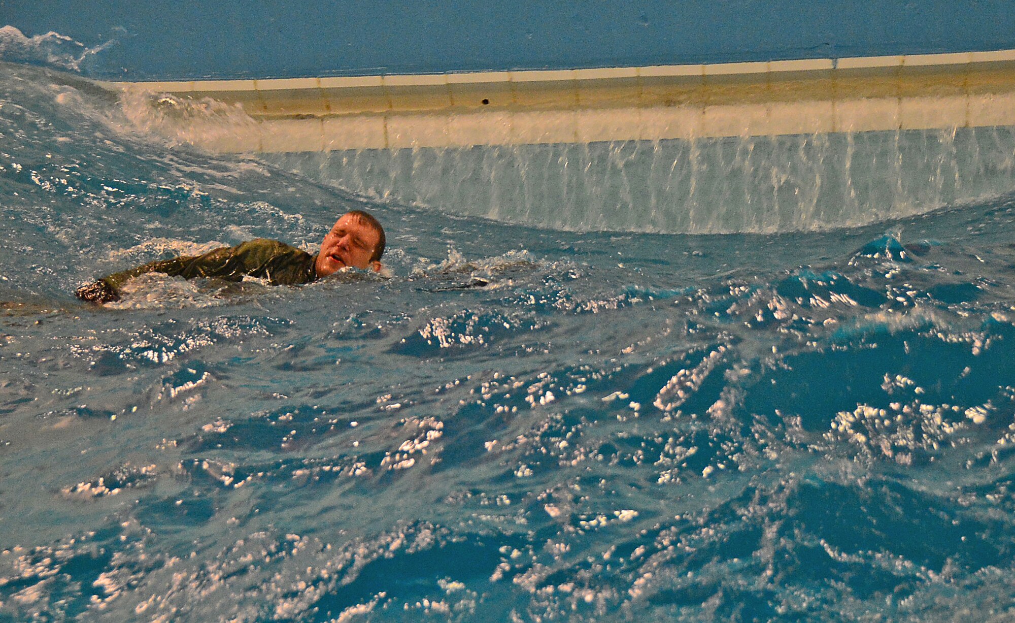 A student of the U.S. Air Force water survival training course swims through 4-foot waves at the Lowestoft College pool in Lowestoft, England, during a course led by survival experts May 22, 2014. The class prepared aircrew for dangerous operating environments created by harsh weather conditions over water. When sea conditions are deemed too hazardous, flight training can be diverted to routes over land, ultimately creating noise heard by local communities. (U.S. Air Force photo by Airman 1st Class Erin O’Shea/Released)