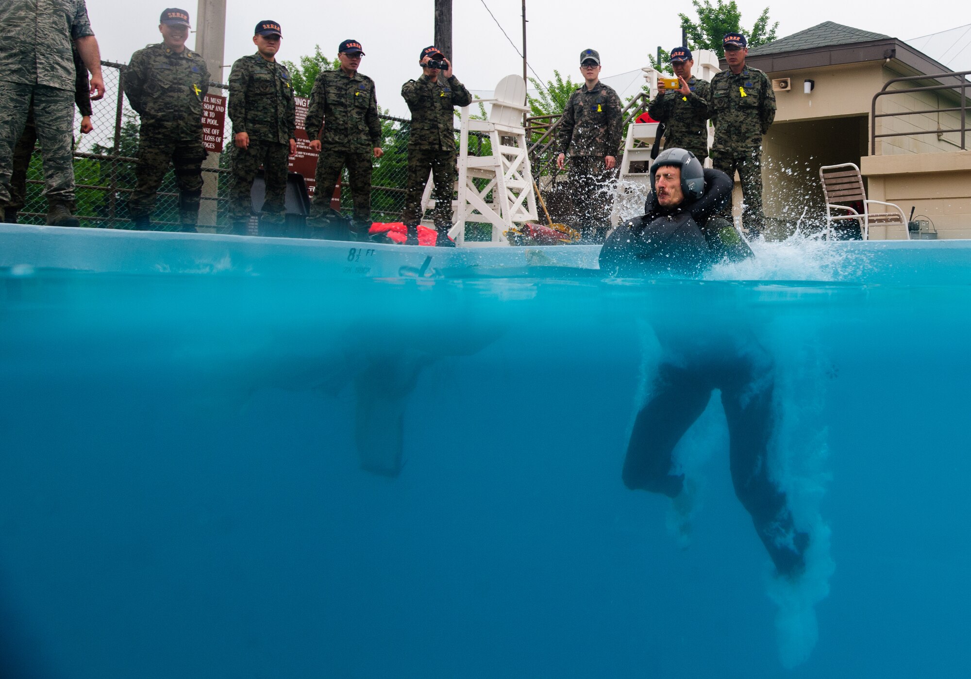Tech. Sgt. Kurtis Douge, 8th Operations Support Squadron survival, evasion, resistance and escape specialist and weapons and tactics NCO in charge, is pulled into the pool as Republic of Korea SERE instructors watch the demonstration at Kunsan Air Base, Republic of Korea, May 20, 2014. Douge and the SERE team hosted the Republic of Korea SERE instructors to share knowledge on water survival training for pilots from both nations. (U.S. Air Force photo by Senior Airman Armando A. Schwier-Morales/Released)