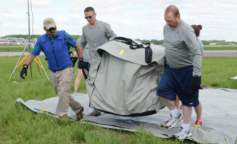 Airmen carry a tent over to the grass during a 976A Patient Decontamination certification at the 115th Fighter Wing in Madison, Wis., May 22, 2014. Once built, the tent provides space for decontamination during chemical, biological, radiological and nuclear emergencies on base. (Air National Guard photo by Senior Airman Andrea F. Liechti)