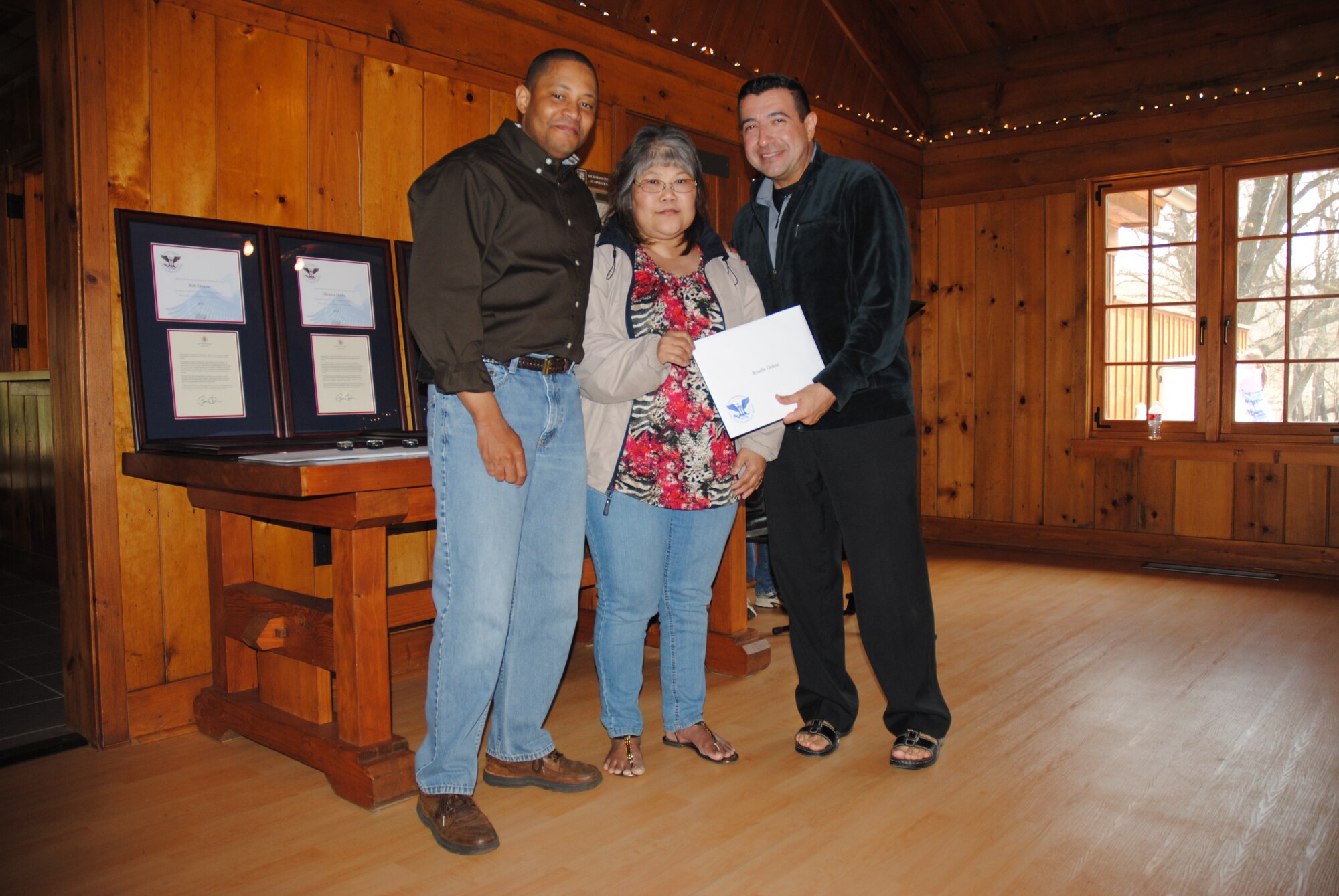 Grand Forks Air Force Base chaplains, Maj. Steven Dabbs and Capt. Ruben Covos, present Roselle Greene with a certificate and bronze lapel pin from the Office of the President of the United States recognizing her as a recipient of a gold level Presidential Volunteer Service Award during a volunteer appreciation picnic held May 17, 2014, at Turtle River State Park, N.D. The gold level award is presented to adults age 25 and older who have donated 500 or more volunteer hours in a 12-month period. Greene donated a total of 2,981 hours. (U.S. Air Force photo/Staff Sgt. Luis Loza Gutierrez)