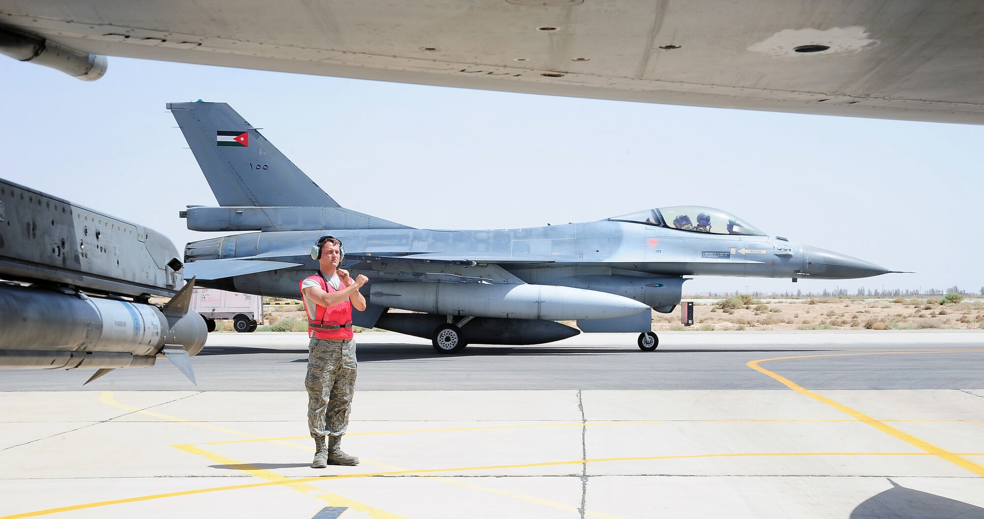 U.S. Air Force Airman 1st Class Blaine Hooten, a crew chief with the 13th Aircraft Maintenance Unit at Misawa Air Base, Japan, marshals a U.S.  F-16 Fighting Falcon while a Royal Jordanian Air Force F-16 taxis for takeoff behind him during Exercise Eager Lion May 27, 2014, at an air base in northern Jordan. This is the fourth year Eager Lion has been hosted by Jordan and with 12,500 participants from more than 20 countries, is larger than last year’s exercise. (U.S. Air Force photo by Staff Sgt. Brigitte N. Brantley/Released)