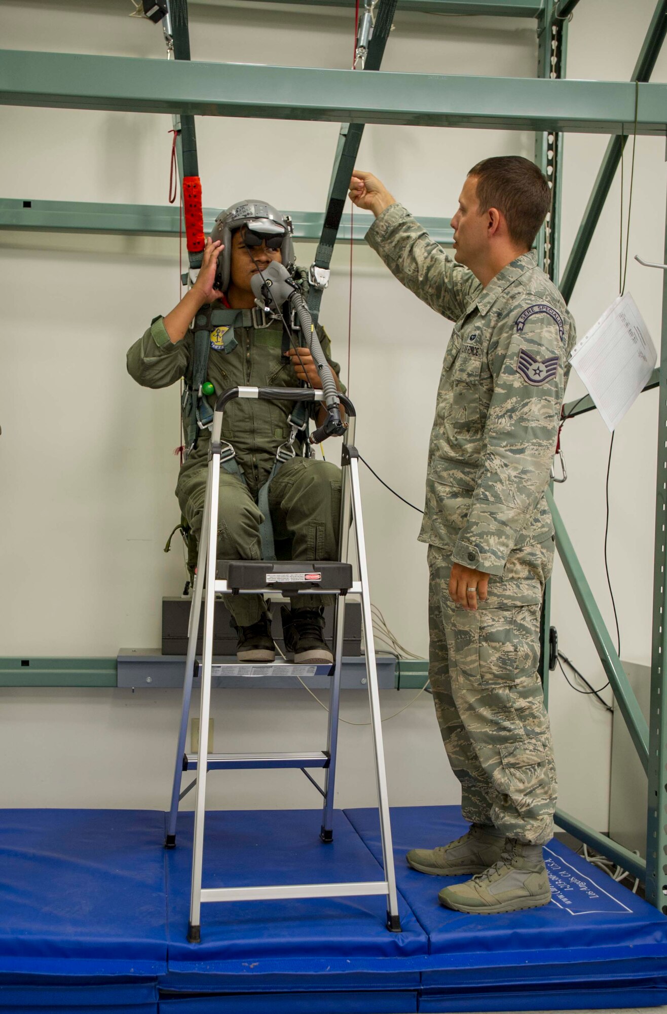 Kirby Balinski, a teenager battling Hodgkin’s Lymphoma, hangs in a virtual reality parachute trainer as Staff Sgt. Jeffrey Ray, 15th Operations Support Squadron survival, evasion, resistance and escape specialist, explains how  to use the equipment to maneuver to the ground after a simulated aircraft ejection during a tour of the 15th OSS Aircrew Flight Equipment section as part of the Pilot For a Day program at Joint Base Pearl Harbor-Hickam, Hawaii, May 29, 2014. (U.S. Air Force photo/Tech. Sgt. Terri Paden)